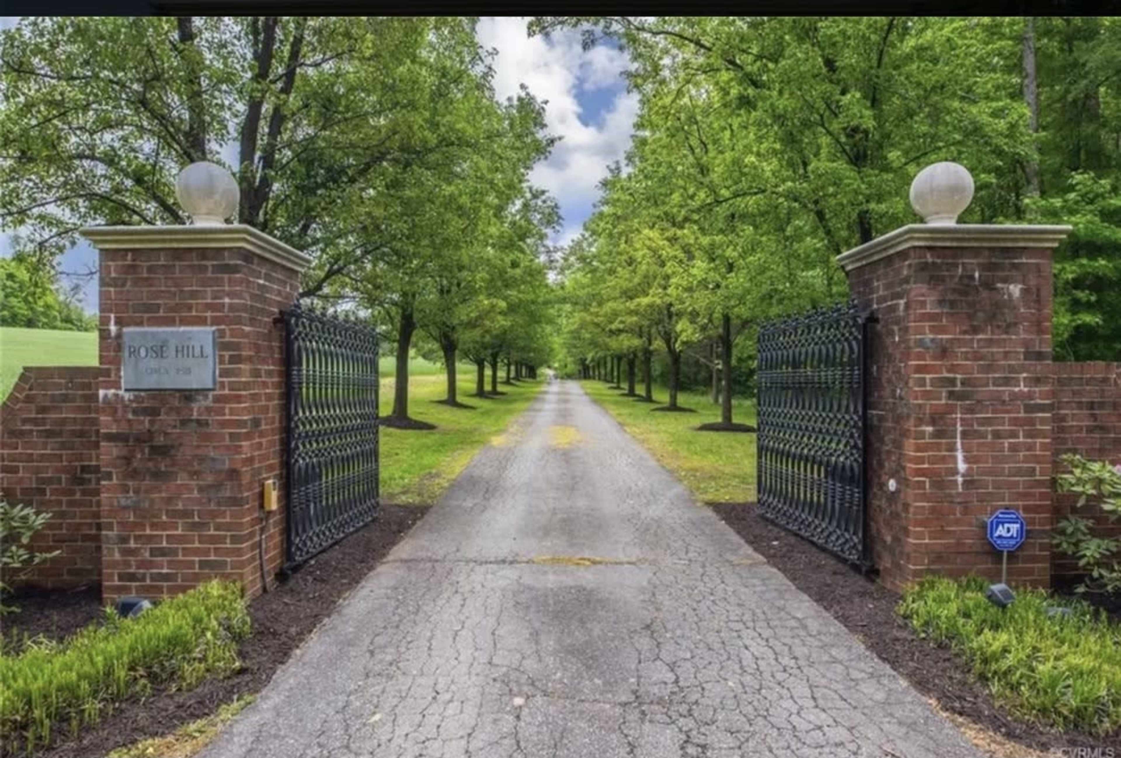 A long, tree-lined driveway leads to an ornate brick gateway with black iron gates marked "Rose Hill."
