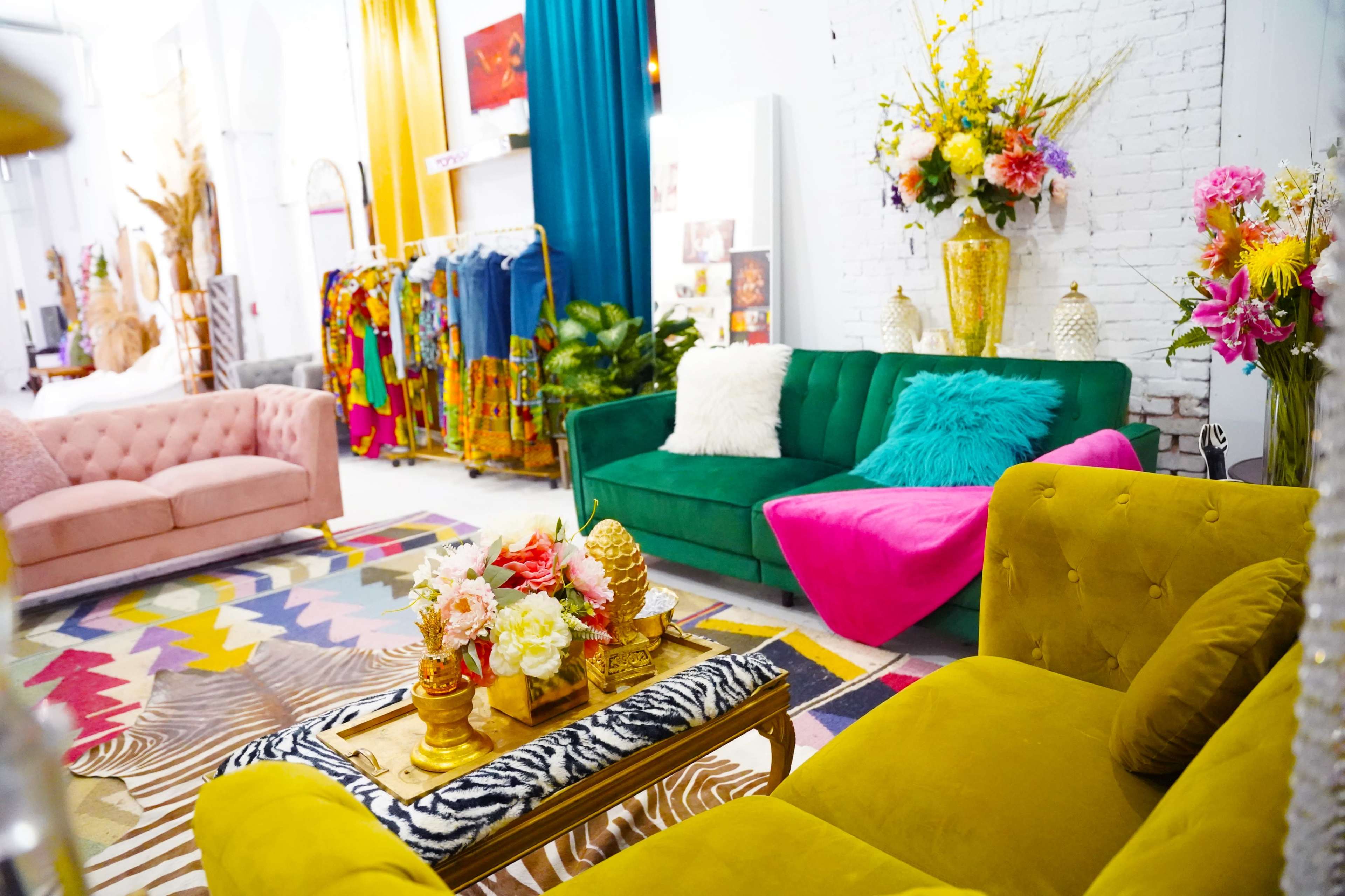A colorful, stylish interior featuring various seating areas with decorative pillows, vibrant floral arrangements, and a bold patterned rug.