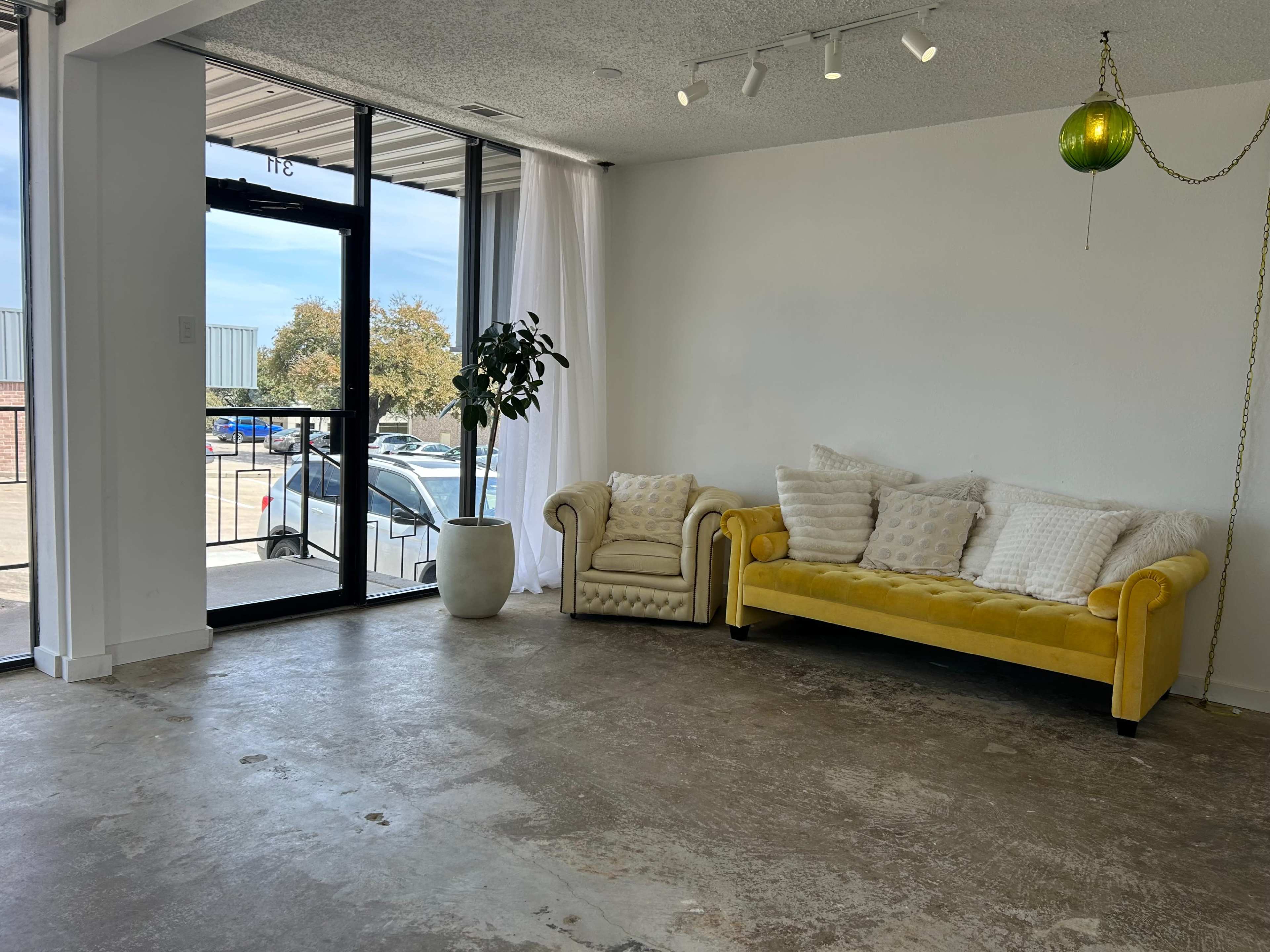 The image shows a bright, minimalist interior with a yellow sofa, a potted plant, and large windows letting in natural light.