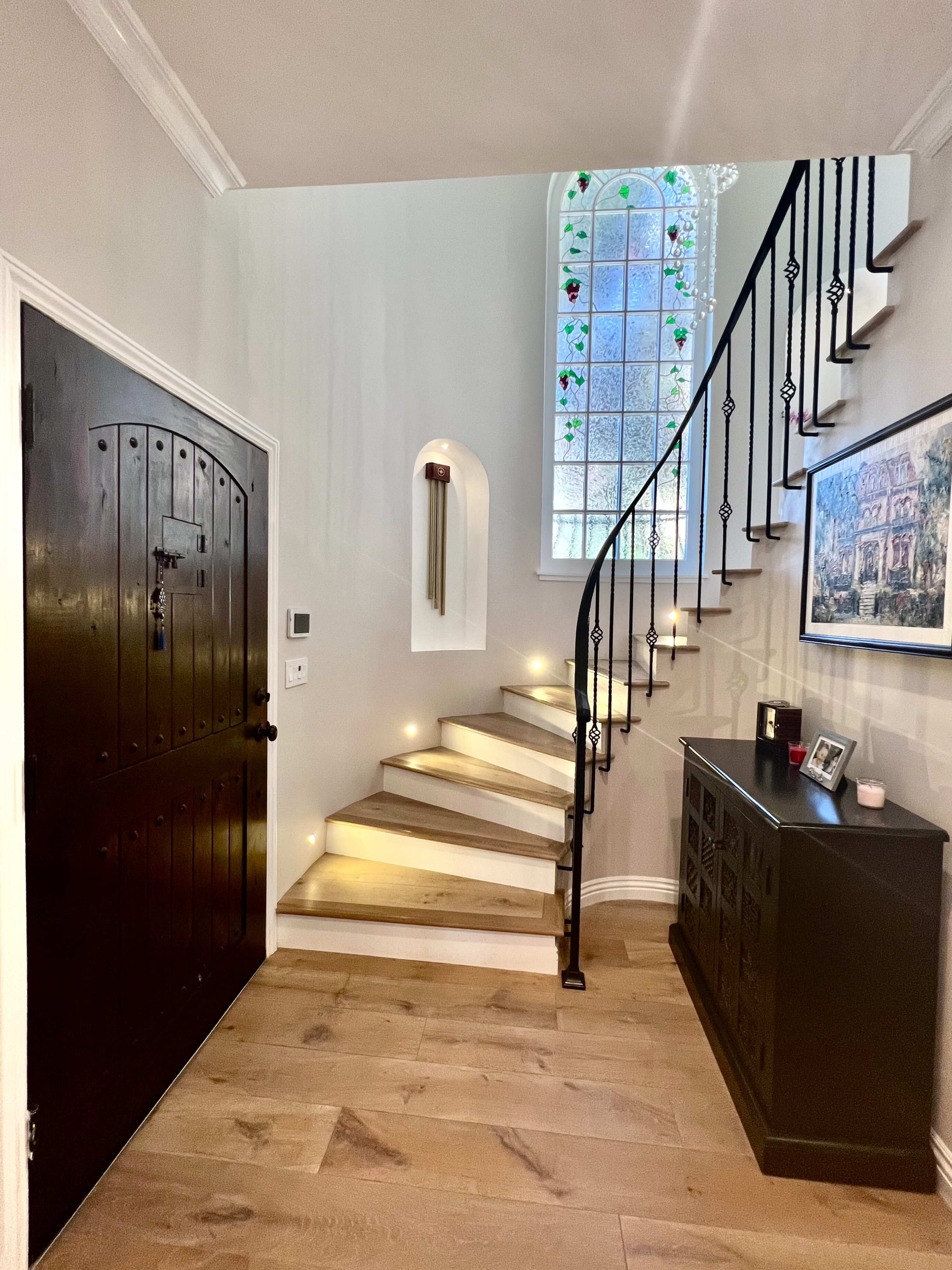 A stairway with illuminated steps leading up to a stained glass window in a well-furnished entryway.