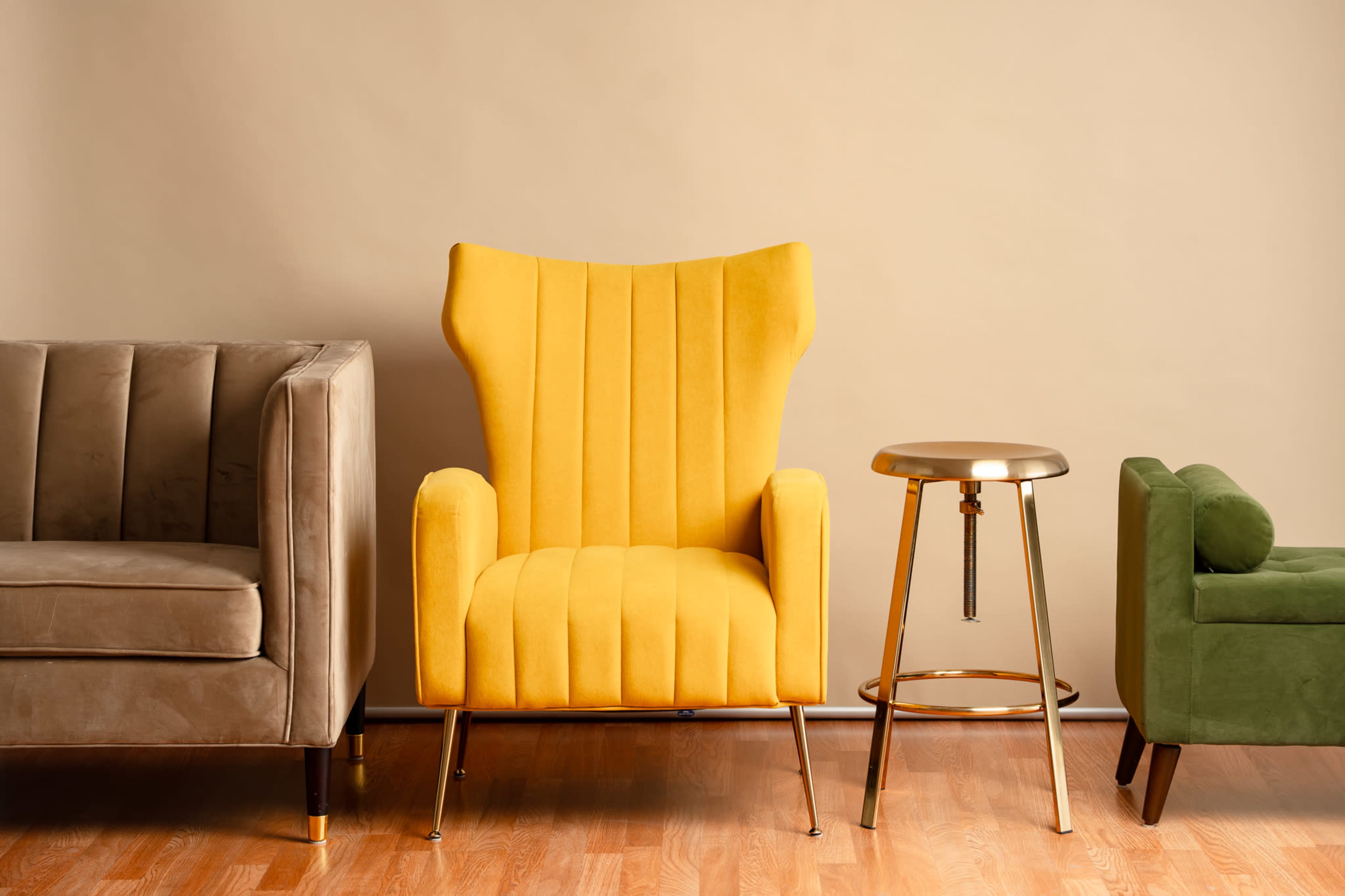 The image features two upholstered sofas and a golden stool arranged against a neutral-colored wall.