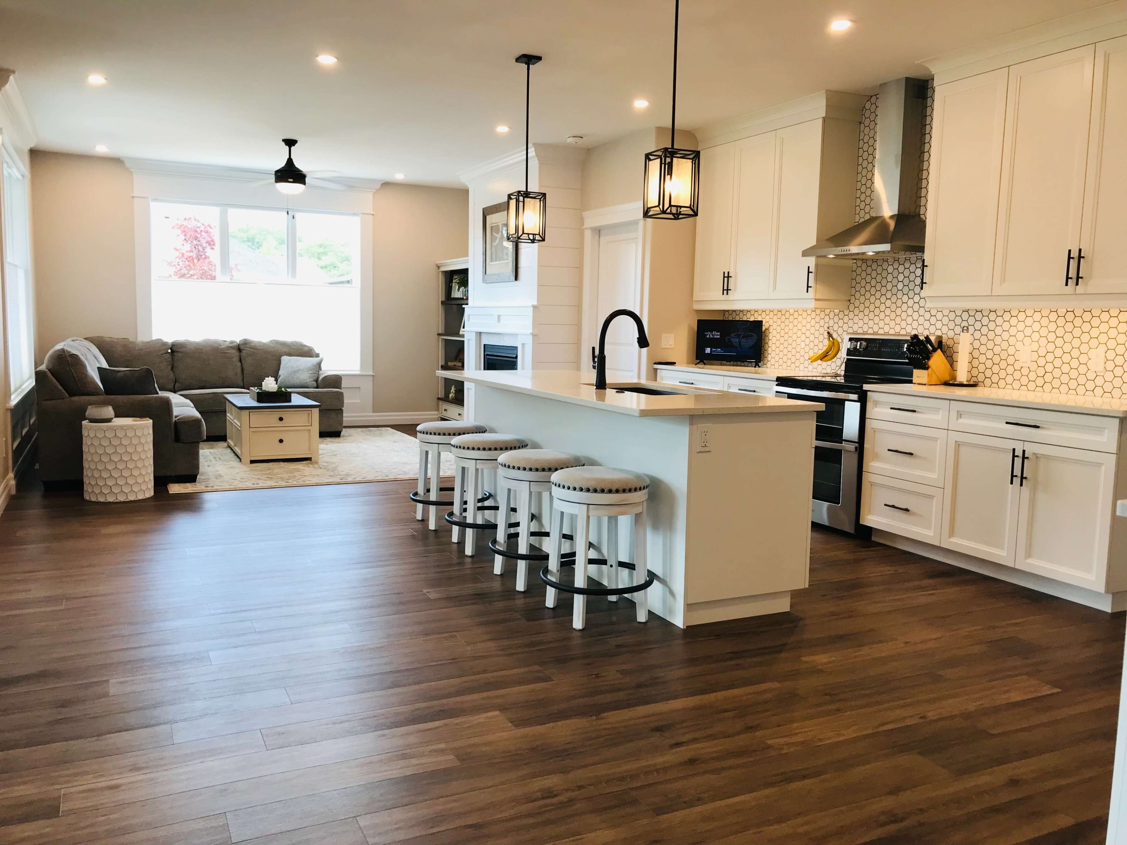 A modern kitchen and living area with white cabinetry, a large island with seating, and a gray sofa beside a window.