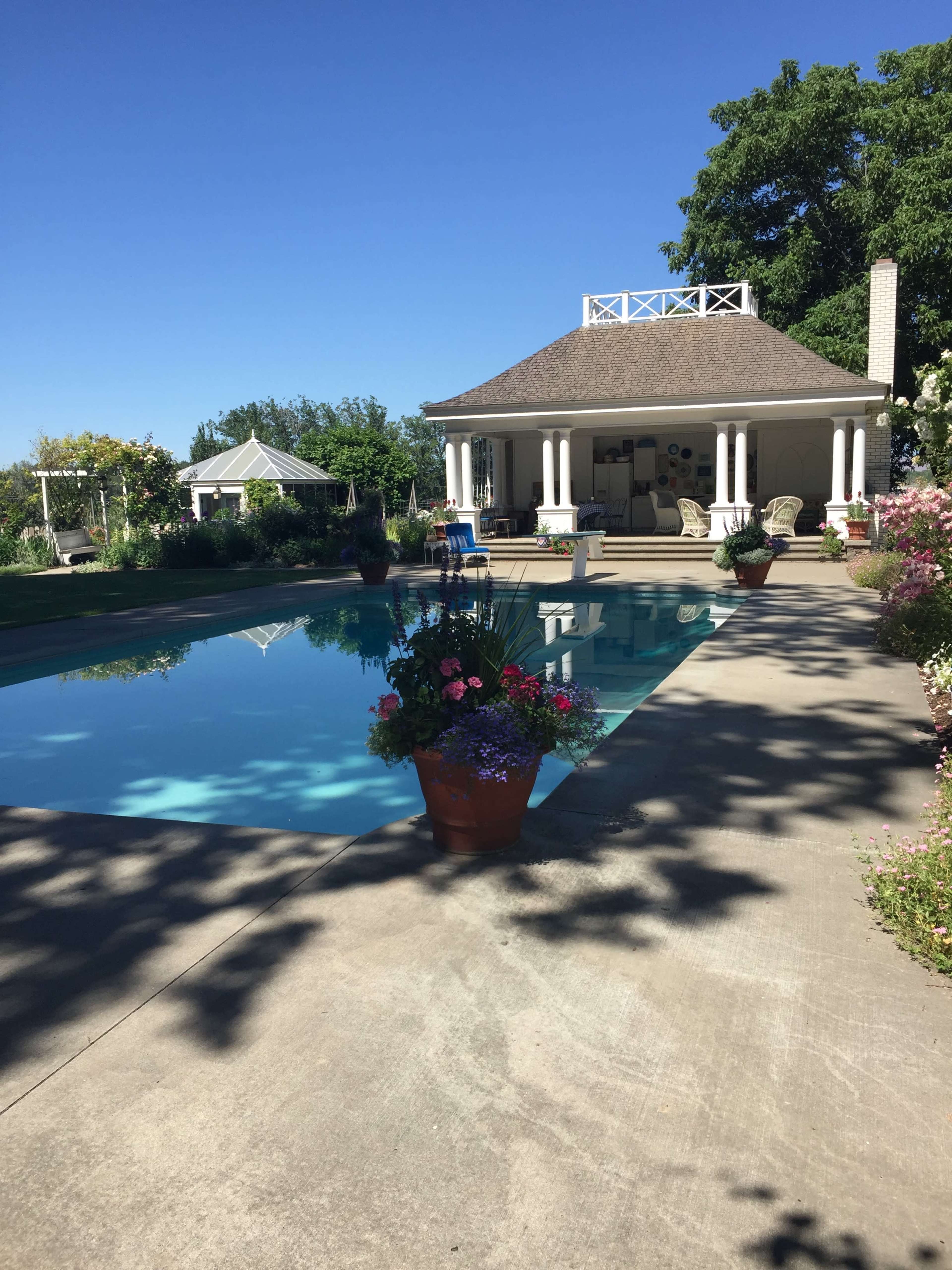 A swimming pool surrounded by a patio, adorned with potted plants, and a gazebo in the background.