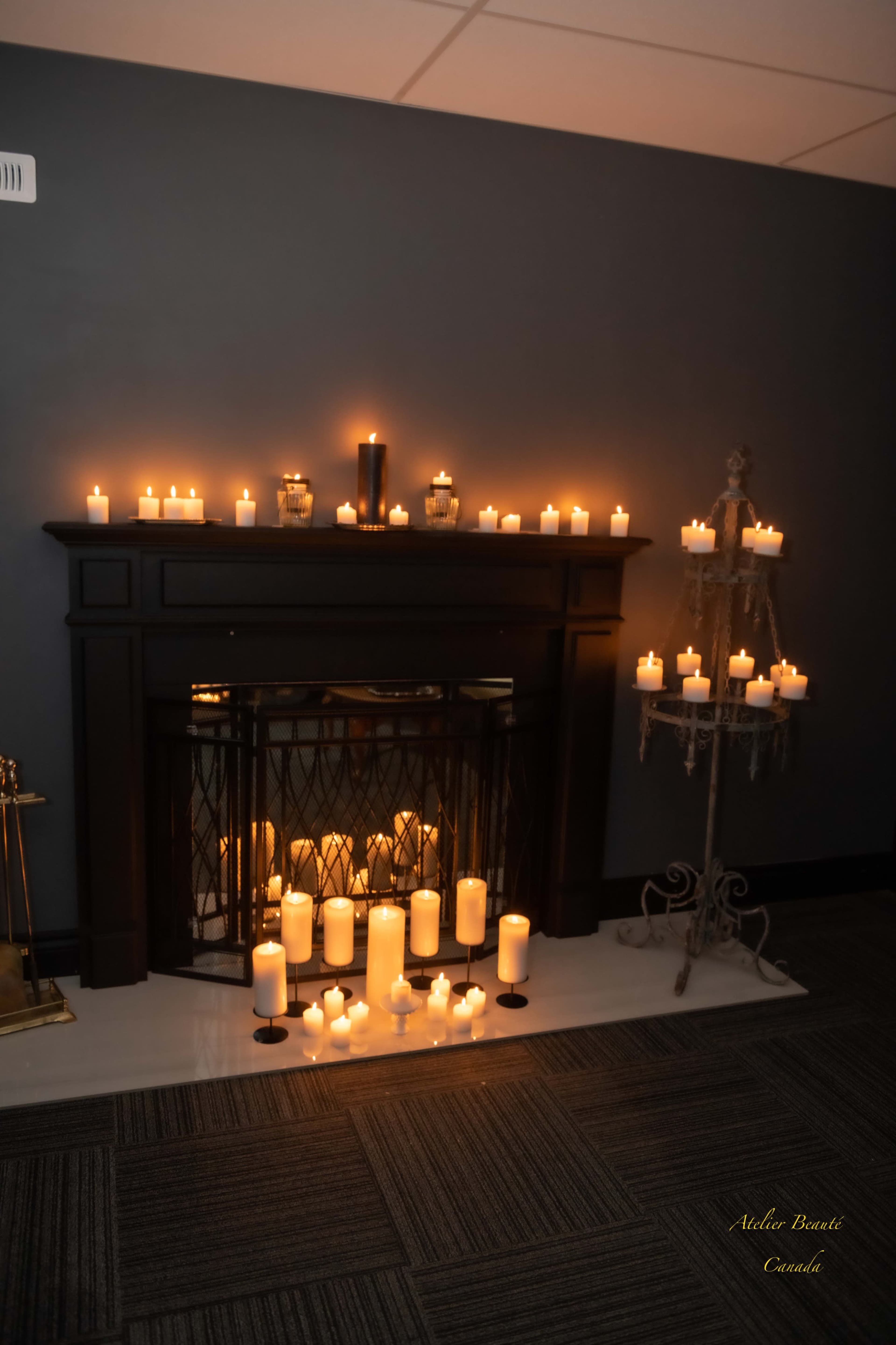 A dark room features a fireplace adorned with numerous glowing candles of varying heights, creating a warm illumination.