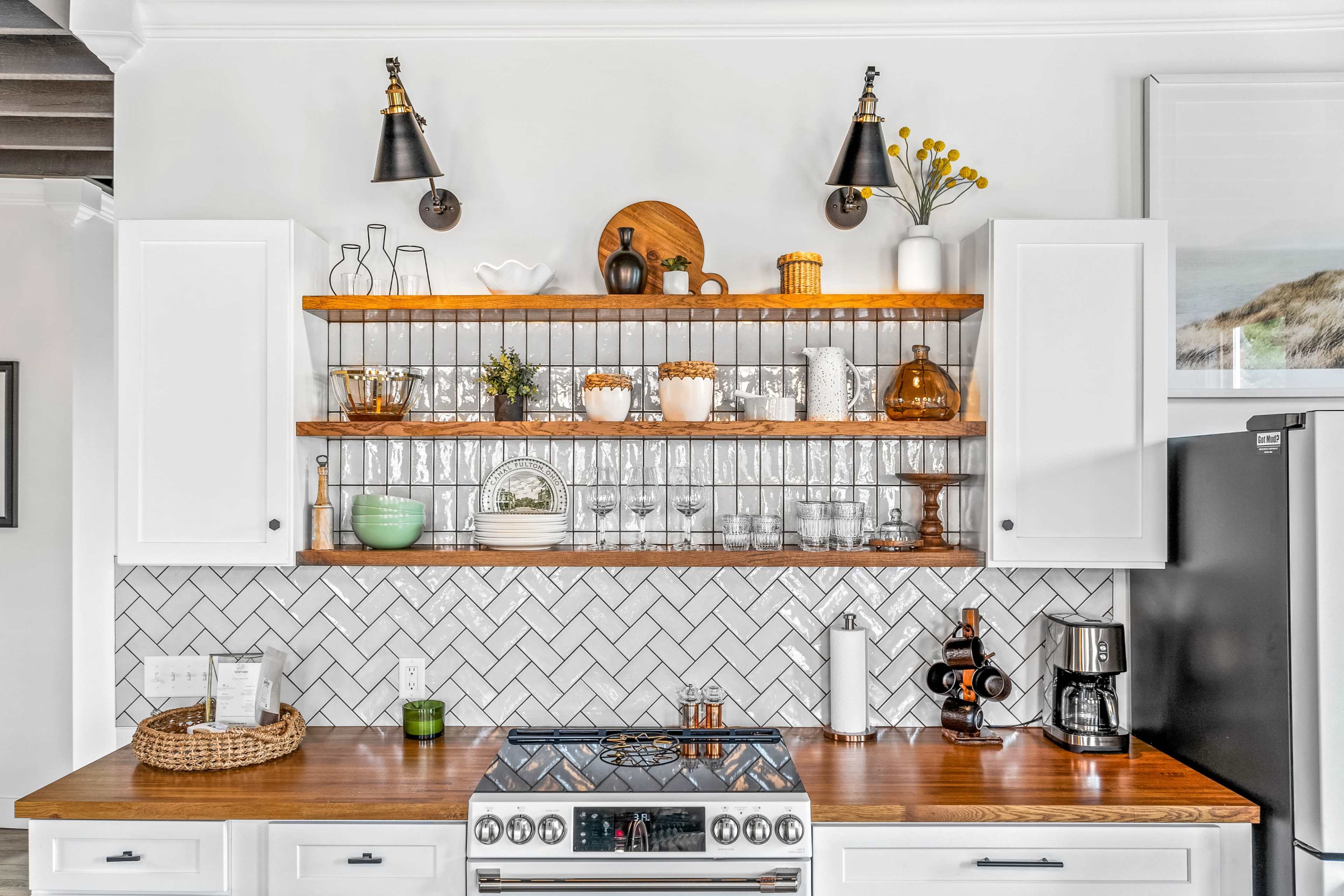 A kitchen with open shelving displaying glassware and decorative items above a wooden countertop with a stove and various kitchen appliances.