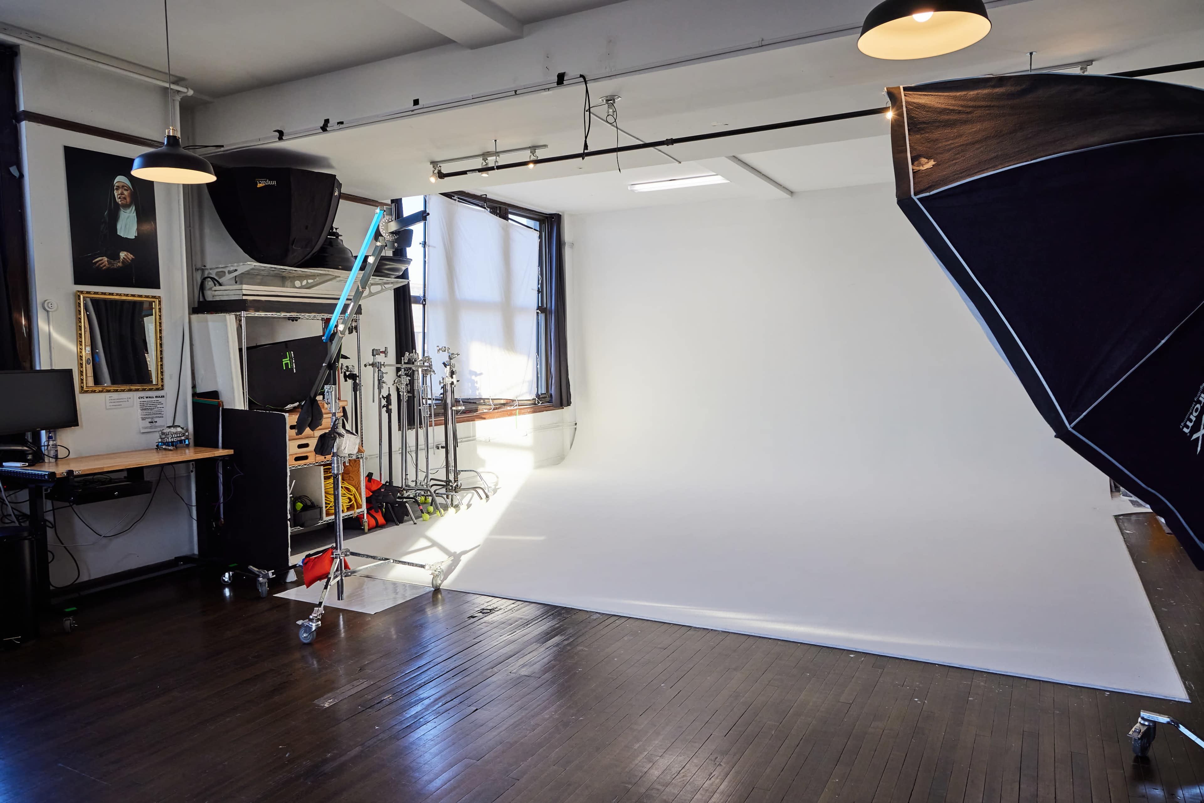 A photography studio with a white backdrop, lighting equipment, and a large window providing natural light.