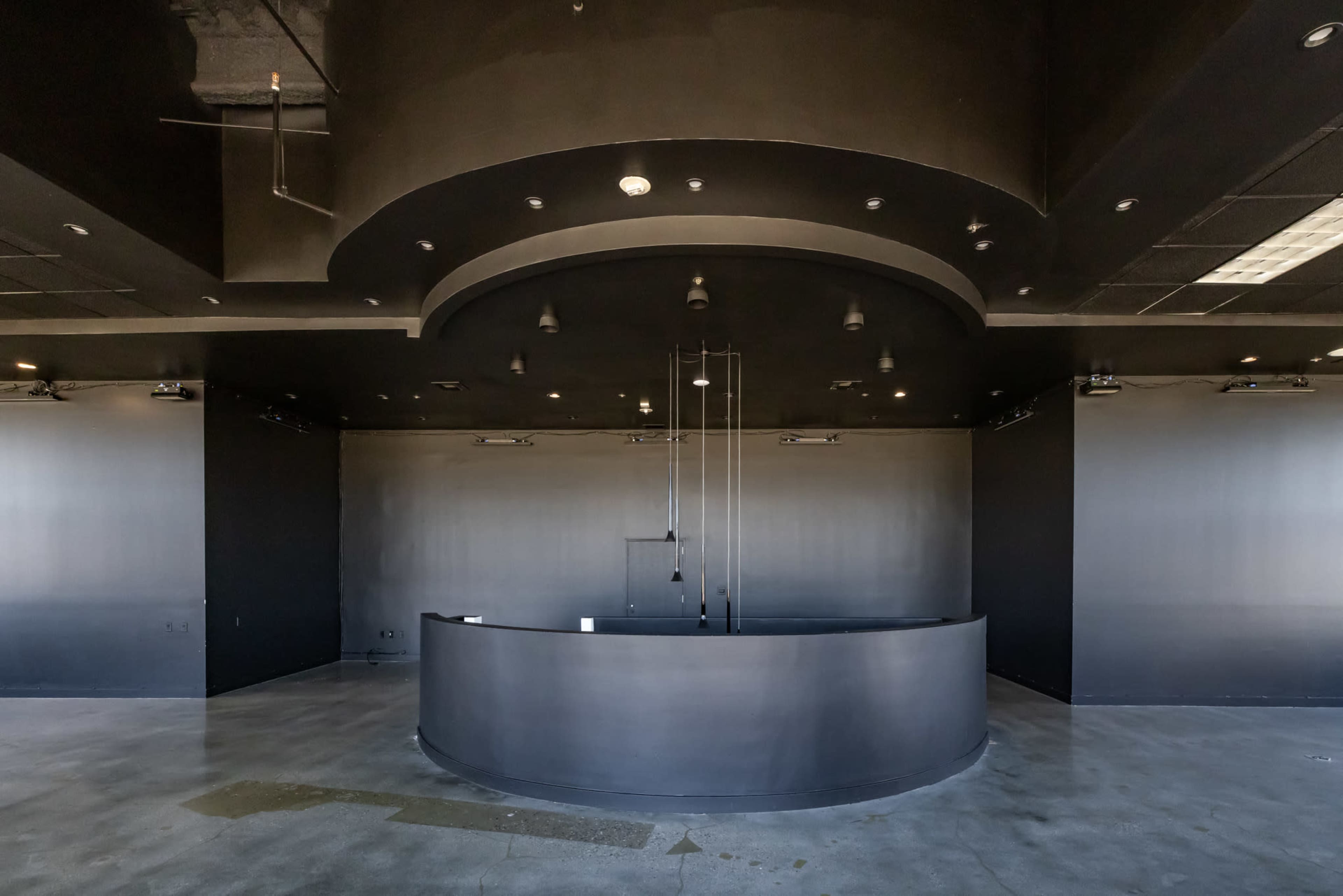 The image shows a minimalist reception area with a curved black front desk, smooth concrete flooring, and dark walls.