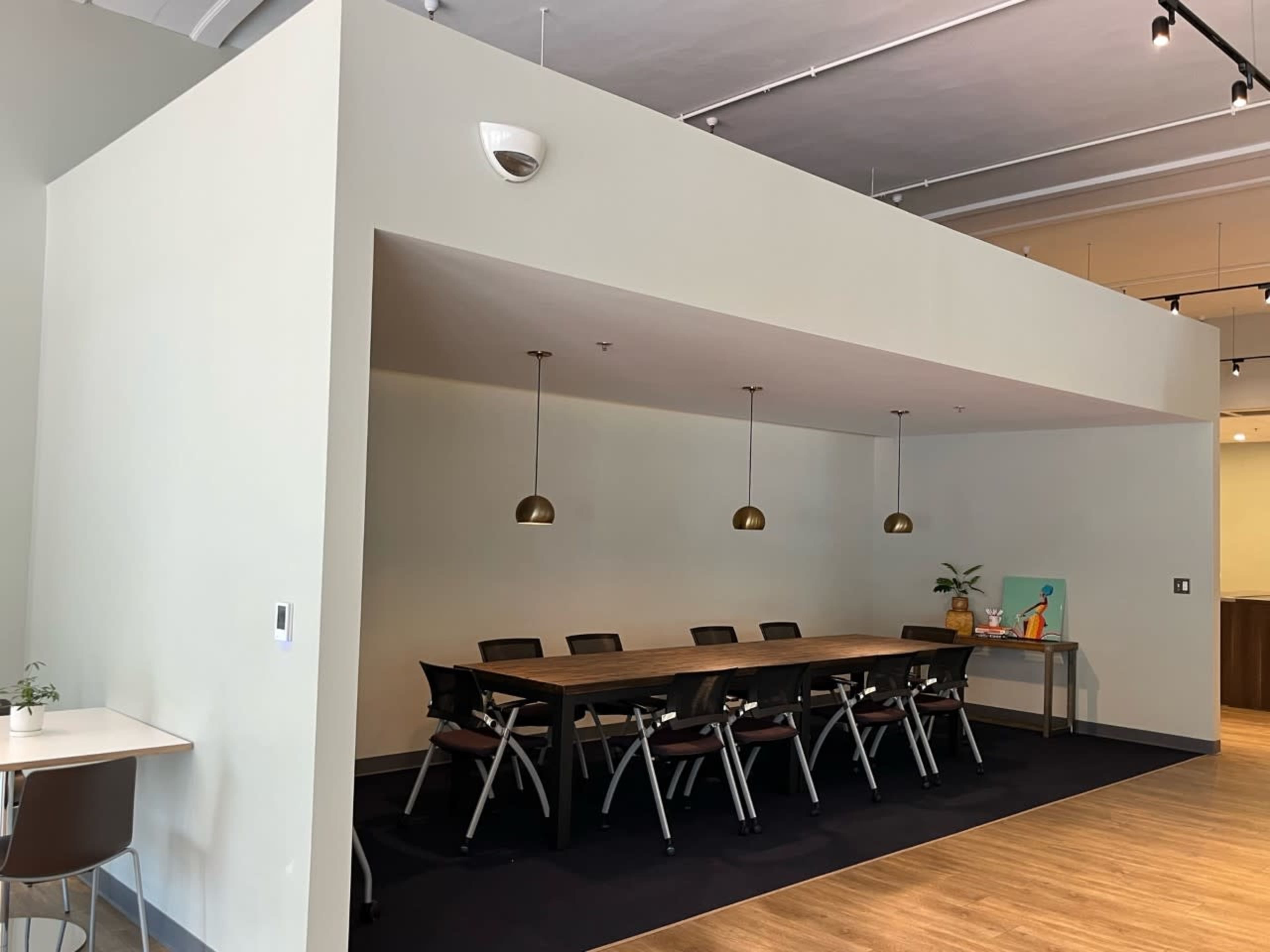 The image shows a spacious meeting room with a long wooden table and several chairs, illuminated by pendant lights.