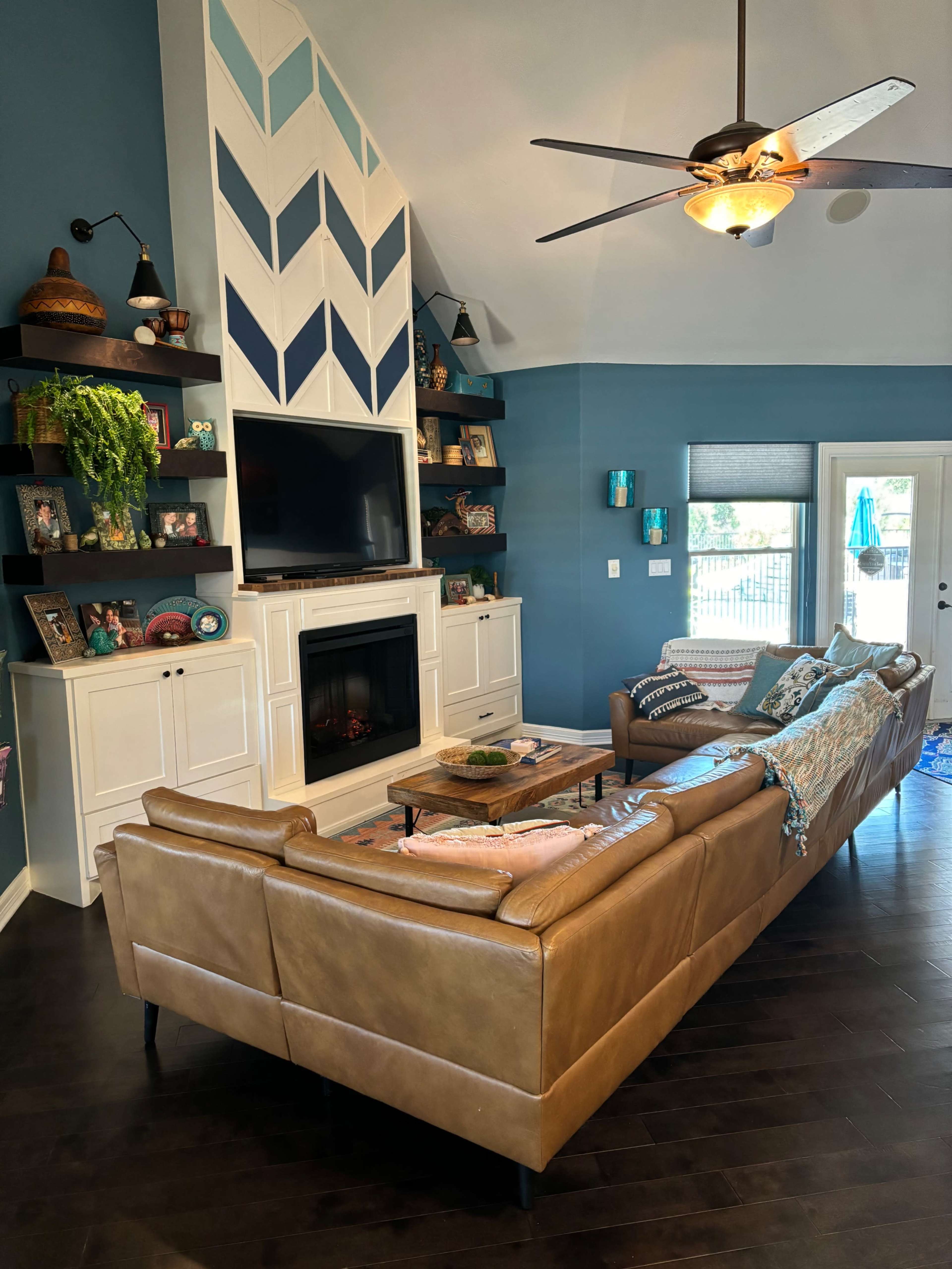 The living room features a large leather sofa, a television mounted above a white fireplace, and a blue accent wall with a patterned design.
