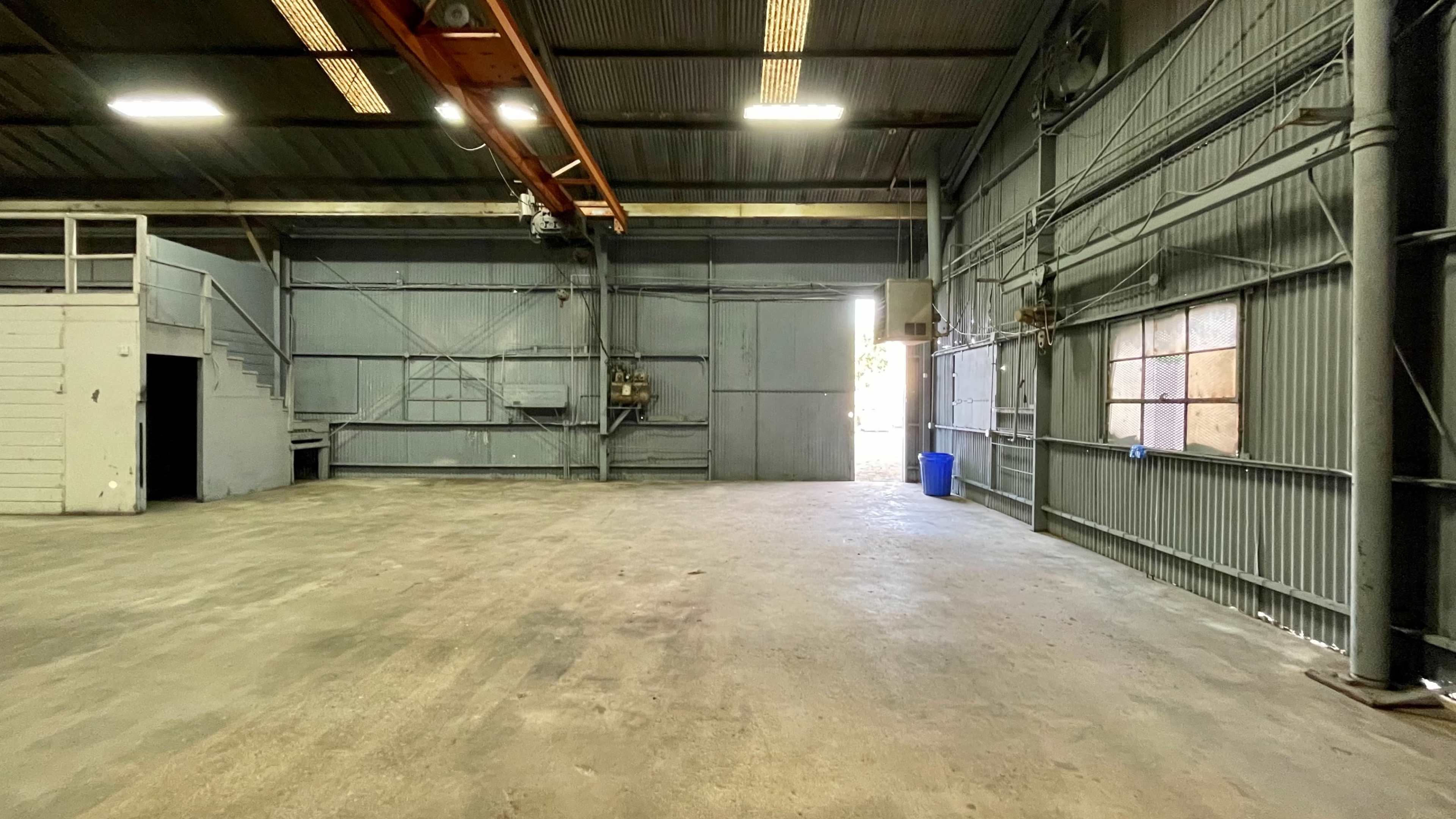 An empty industrial warehouse space with concrete flooring, metal walls, and an open doorway leading outside.