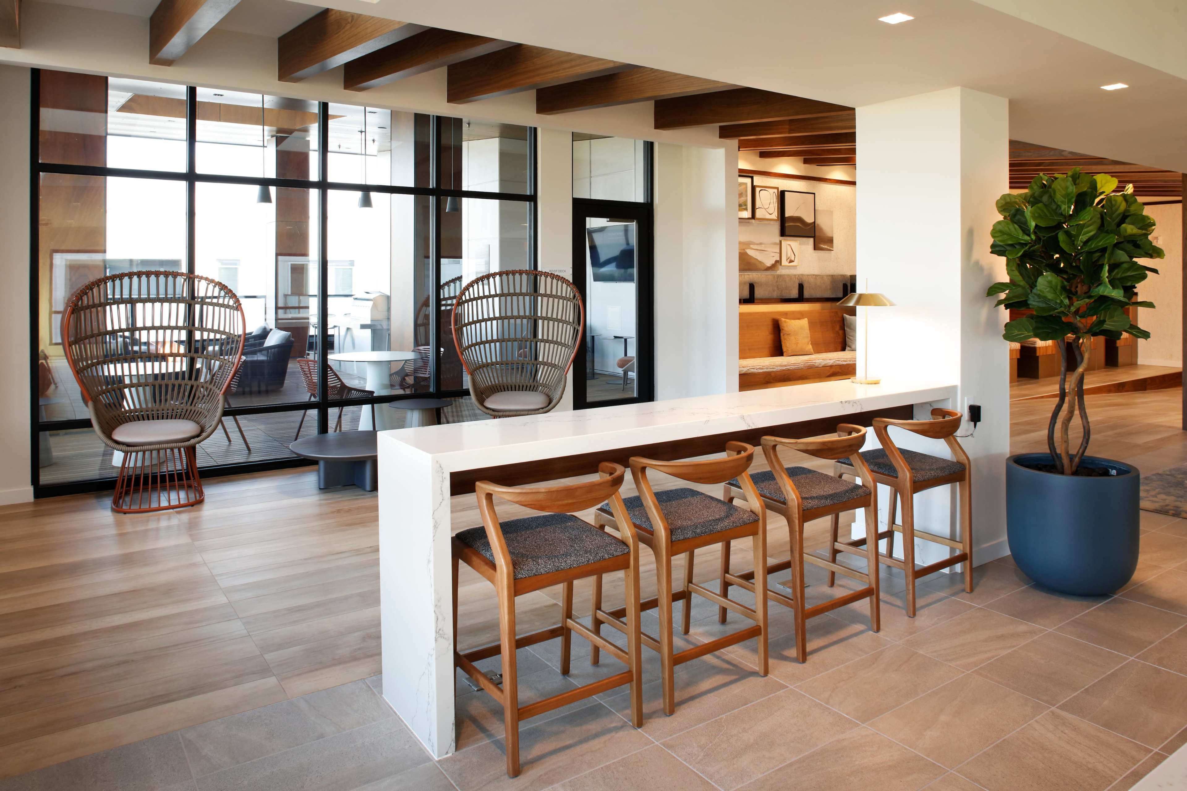 A spacious interior features a counter with four wooden bar stools, surrounded by large windows and modern wicker chairs.
