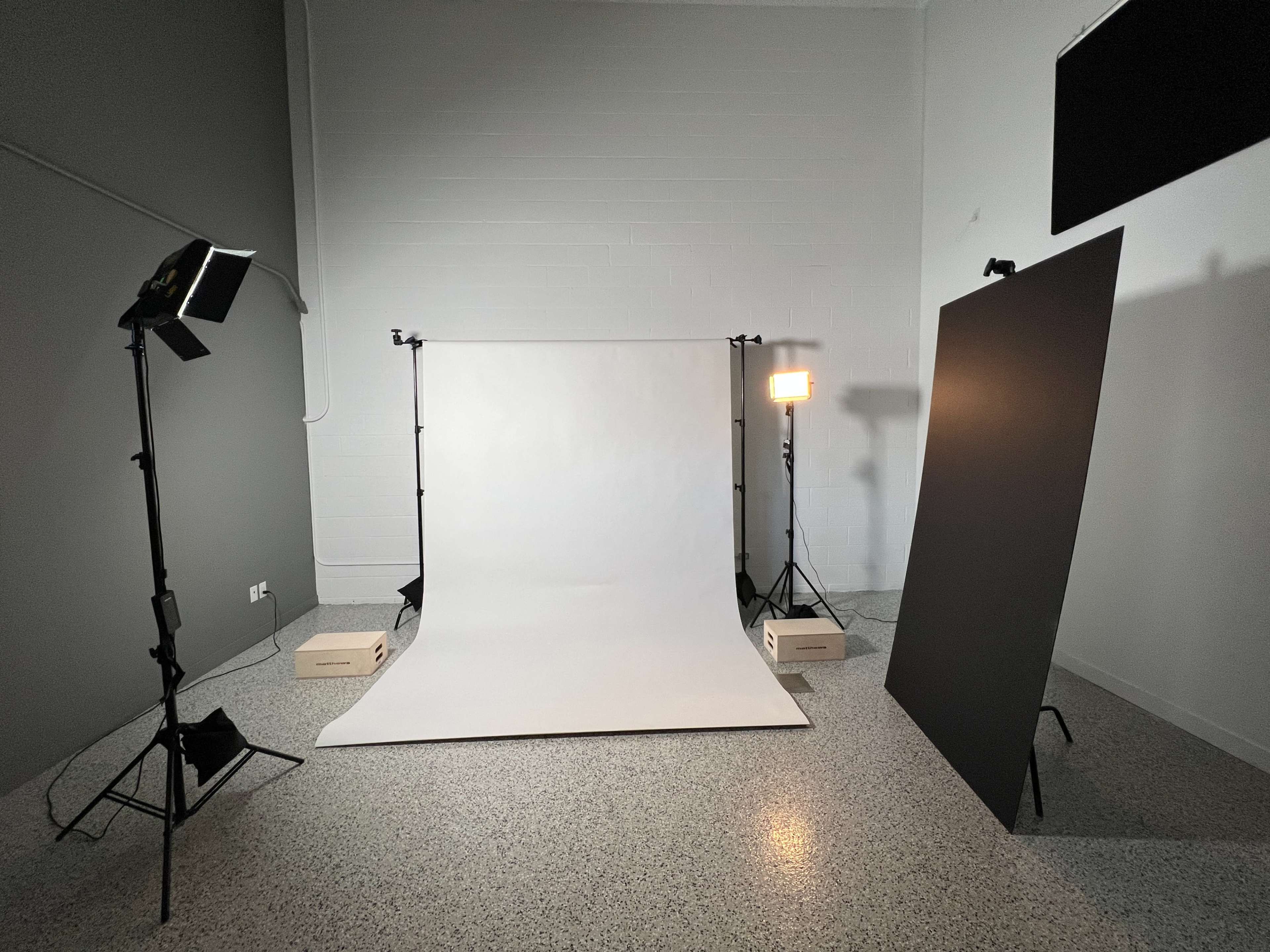 A photography studio setup with a white backdrop, softbox lights, and a black panel on the side.