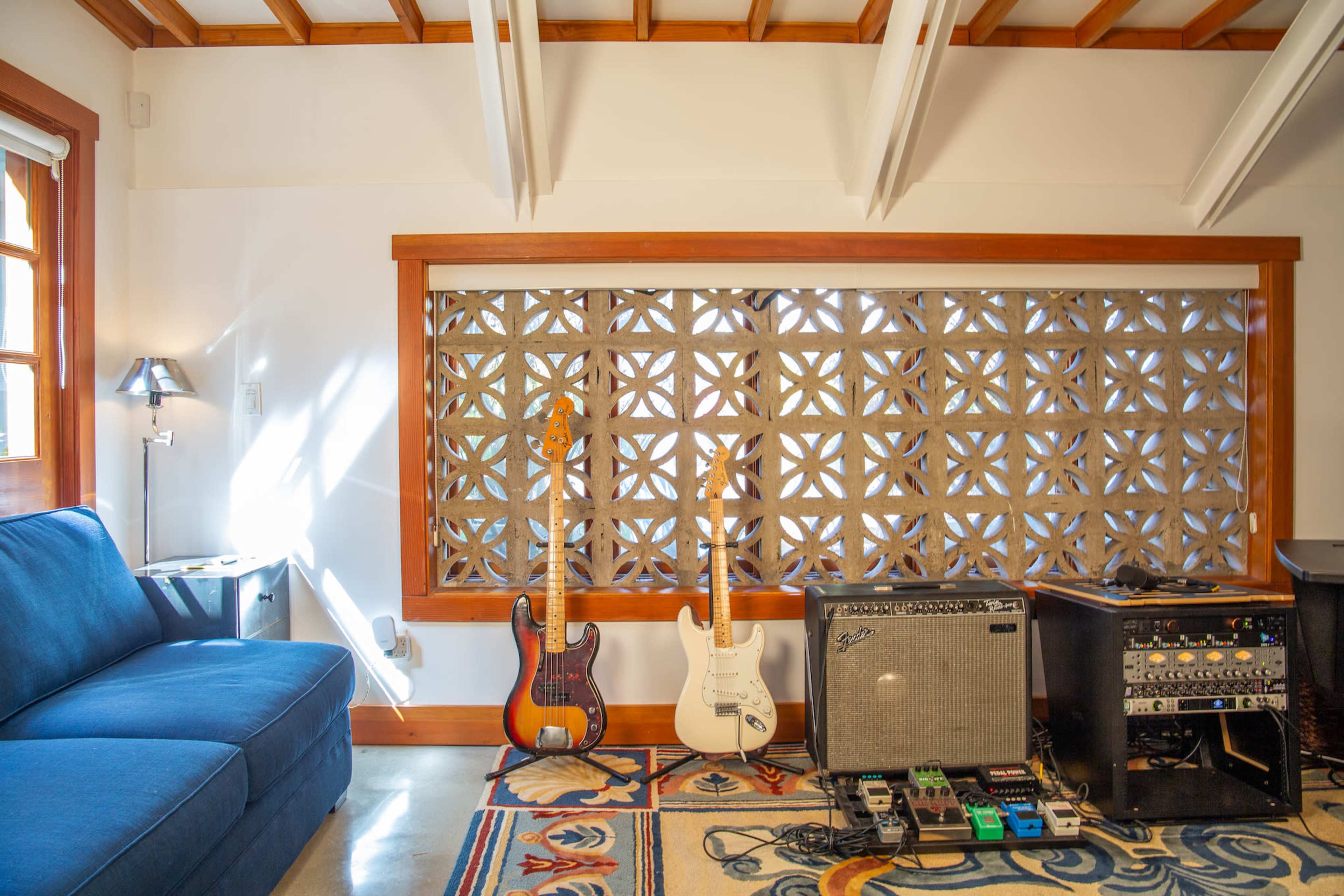 A blue sofa is positioned near a window featuring decorative blocks, with two guitars and an amplifier resting on a patterned rug.