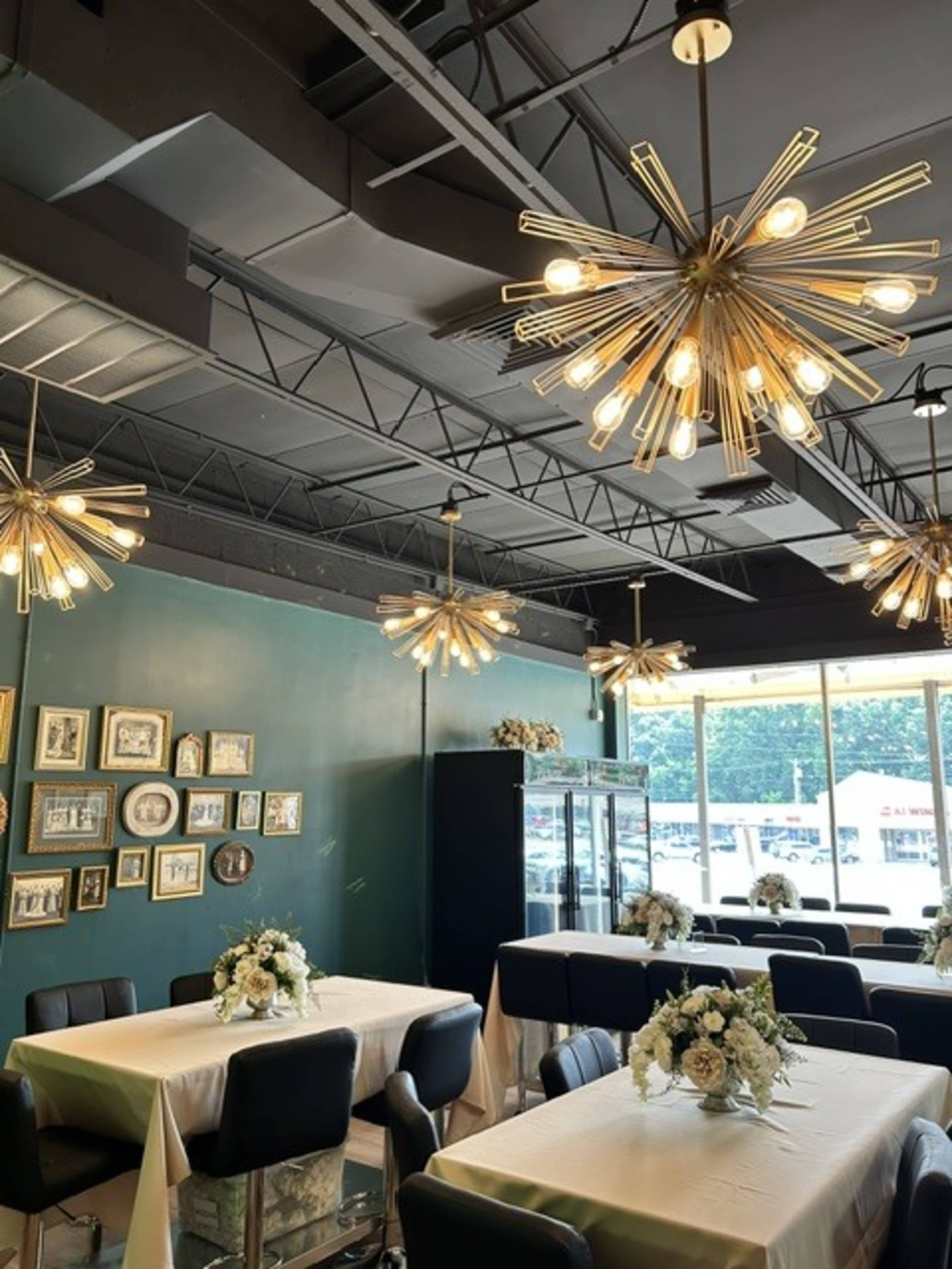 The interior of a restaurant features tables set with floral centerpieces, starburst pendant lights hanging from the ceiling, and a green accent wall decorated with framed pictures.