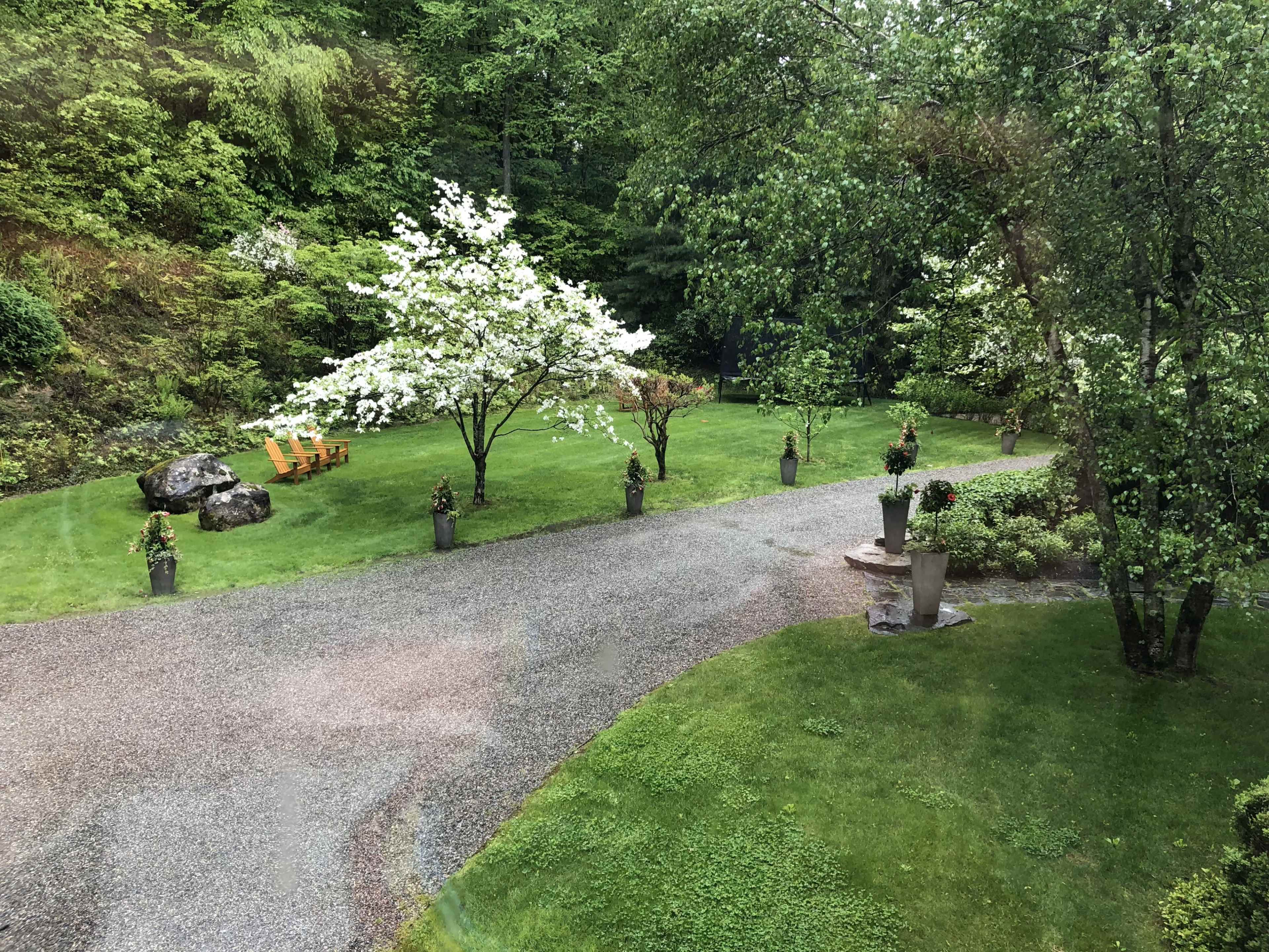 The image shows a landscaped garden with flowering trees, neatly trimmed grass, and decorative planters along a gravel pathway.