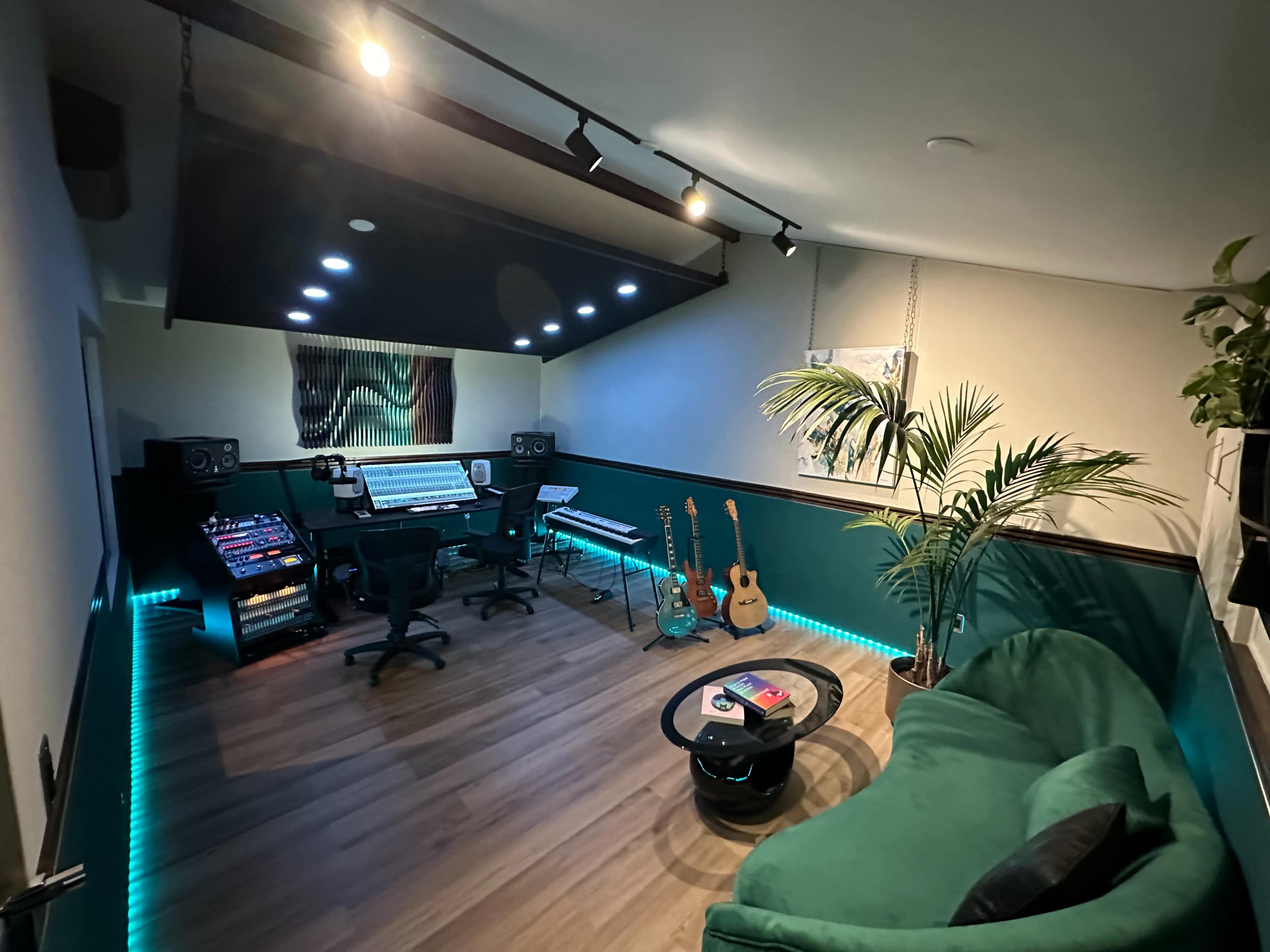 A music studio featuring a mixing console, musical instruments, and a lounge area with a green sofa and plants.