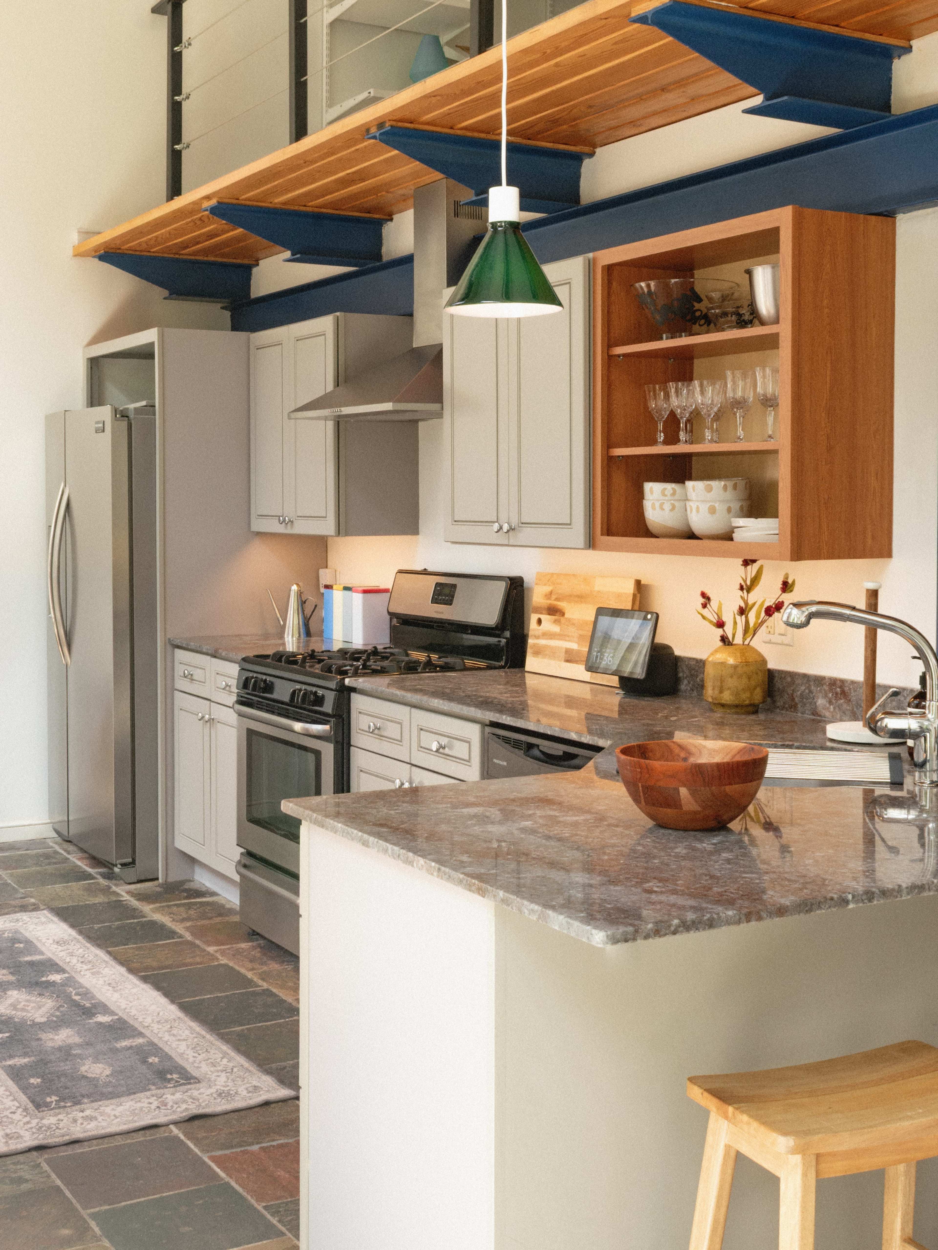 The image shows a modern kitchen featuring gray cabinetry, stainless steel appliances, and a large island with a granite countertop.