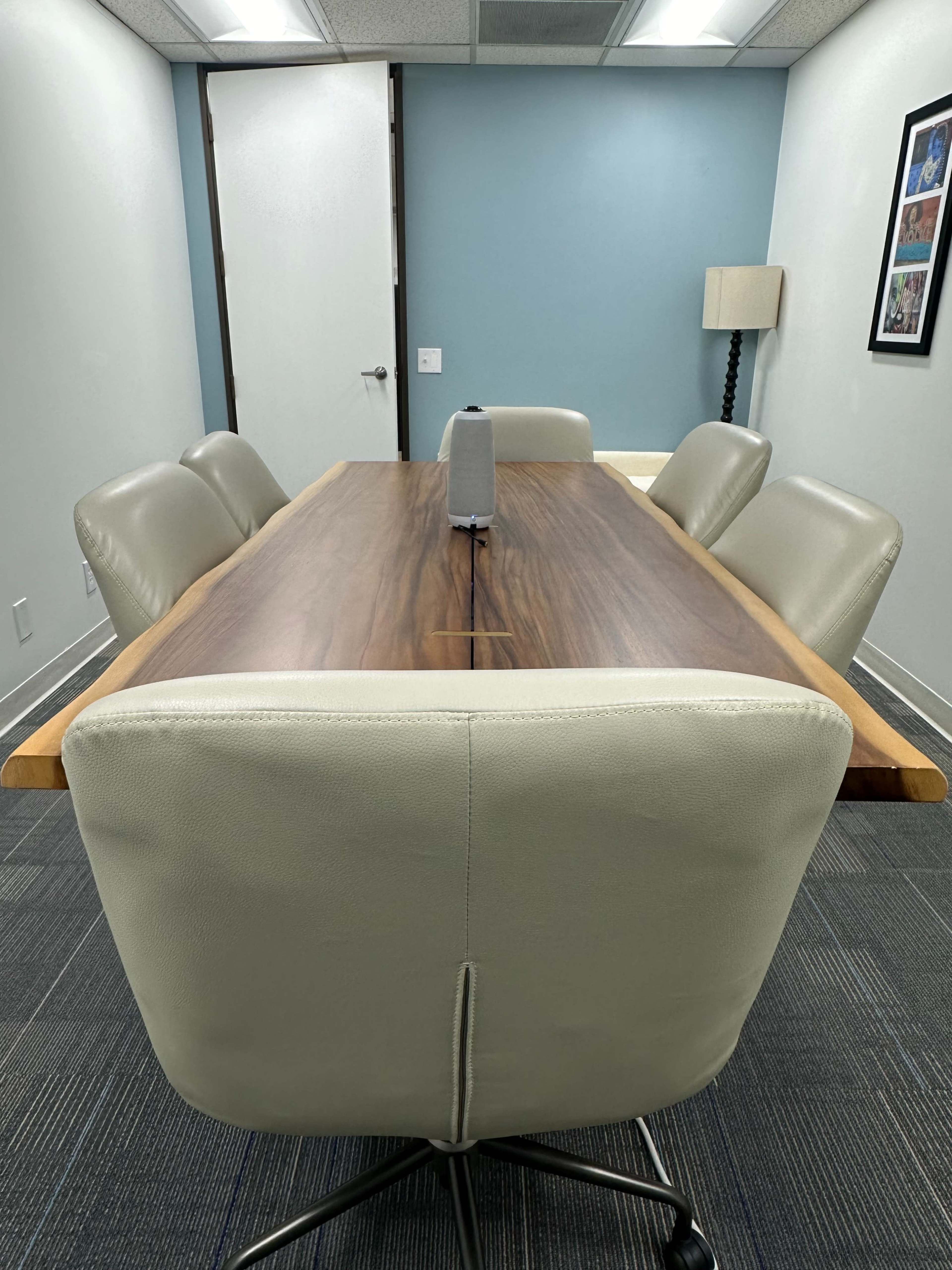 A conference room features a long wooden table with a central microphone and leather chairs arranged around it.