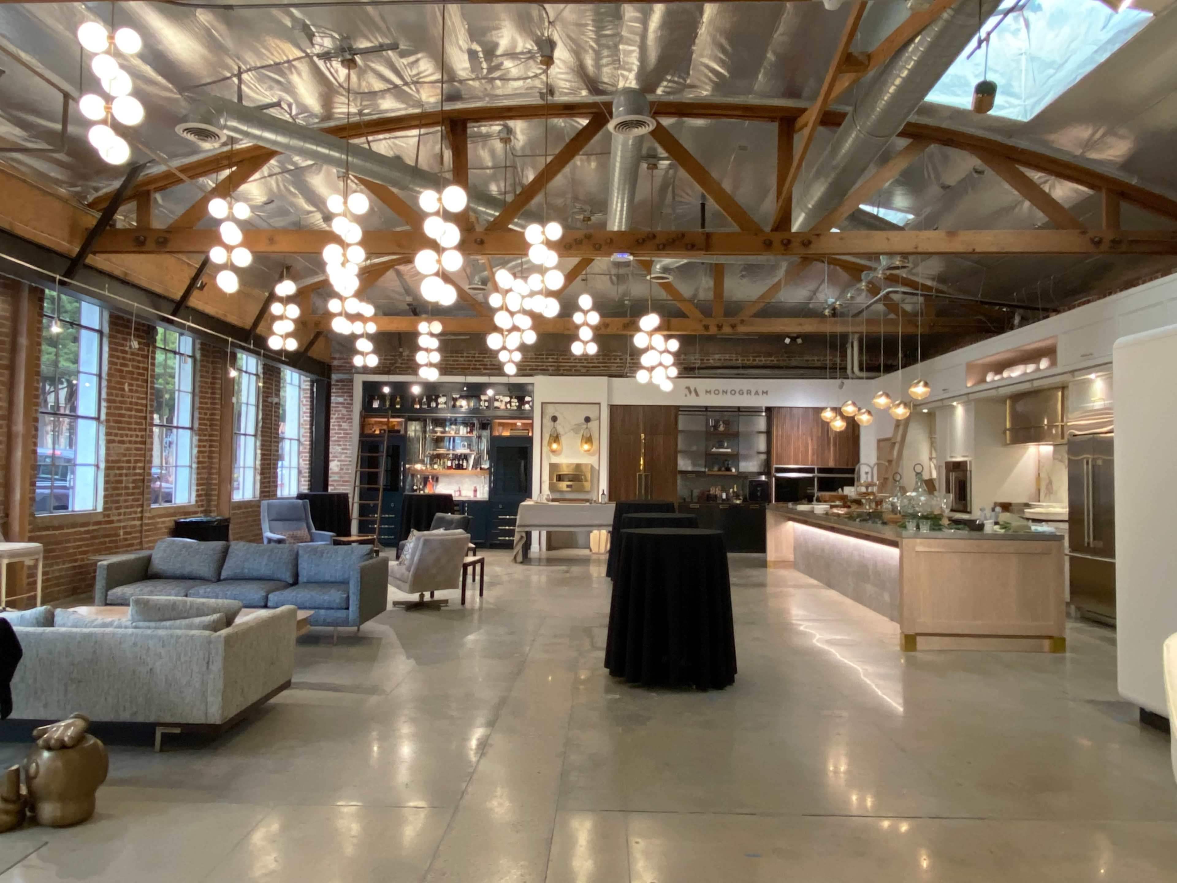 A spacious interior with modern decor, featuring seating areas, a long countertop with kitchen appliances, and pendant lighting hanging from a high ceiling.