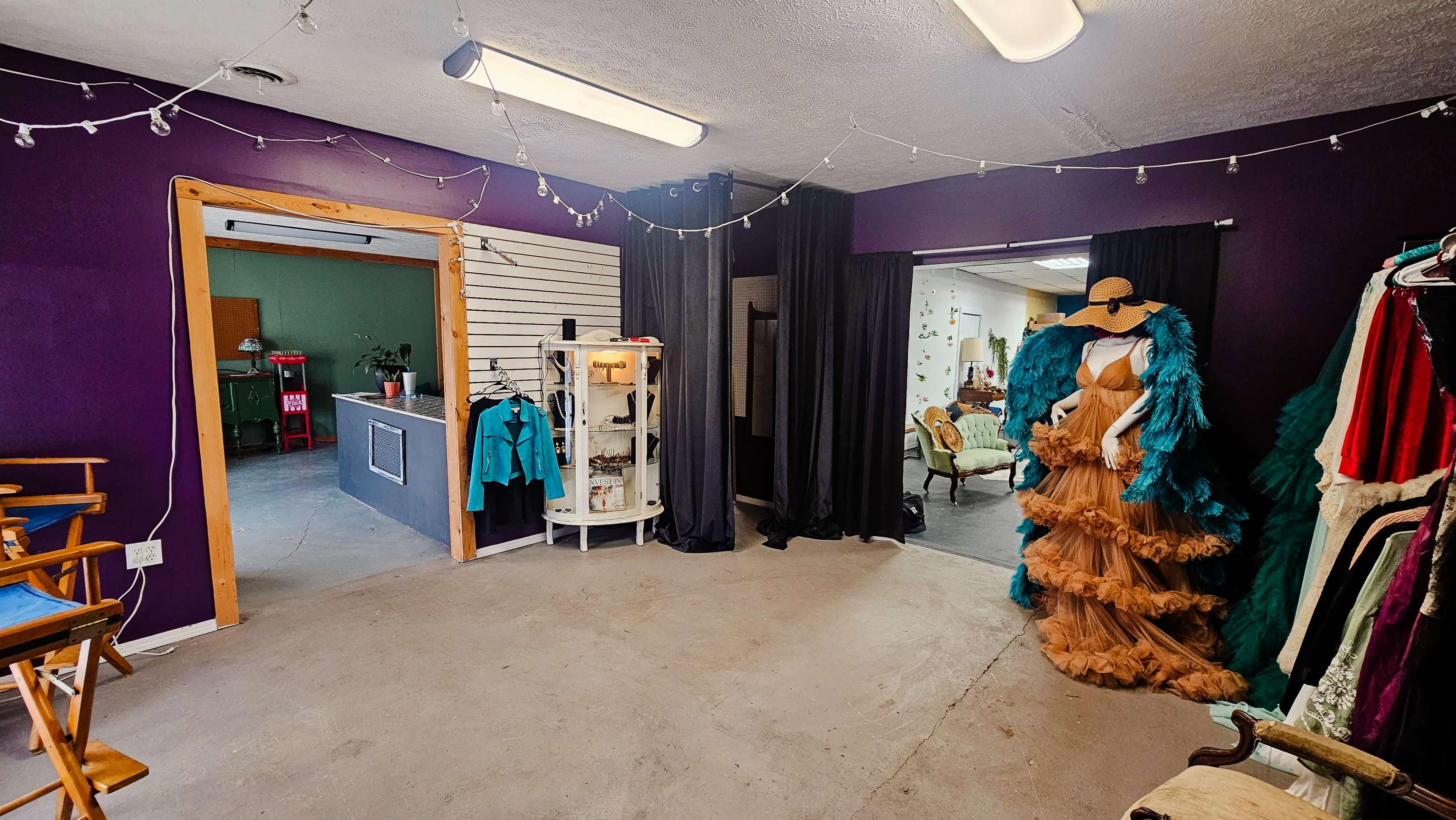 The image shows a room with a purple wall, featuring mannequins dressed in colorful outfits, a display case, and a doorway leading to another space.