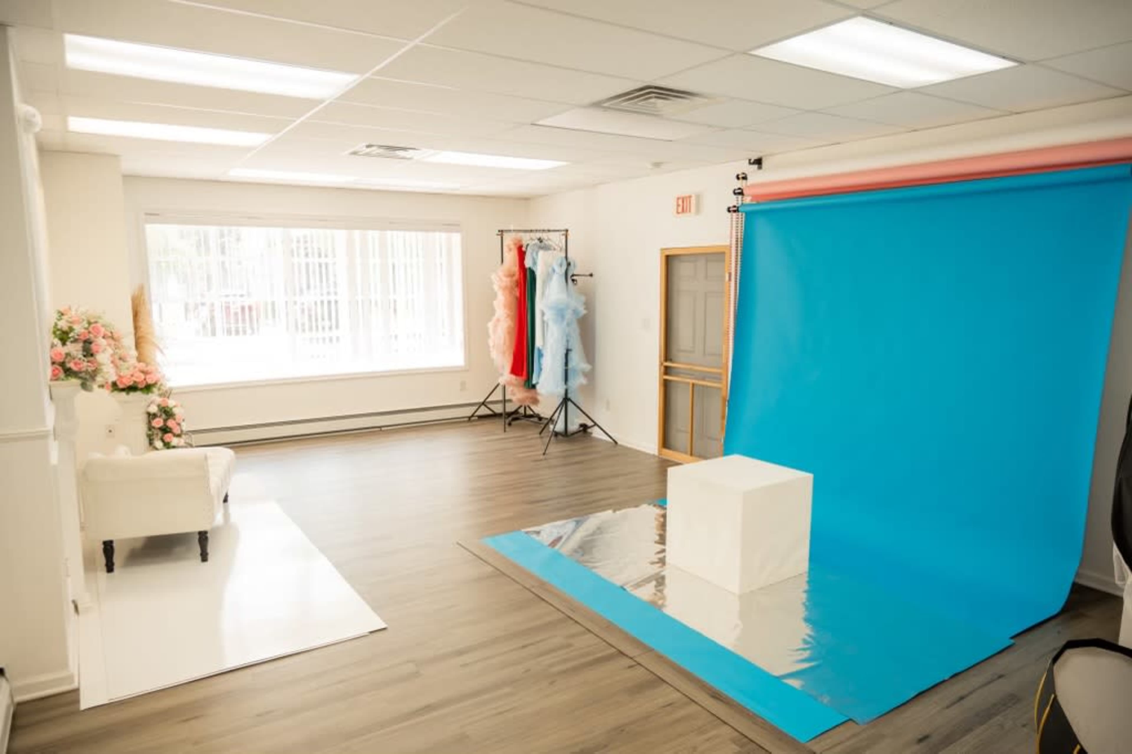 A photography studio with a blue backdrop, a white pedestal, and clothing racks with colorful garments.
