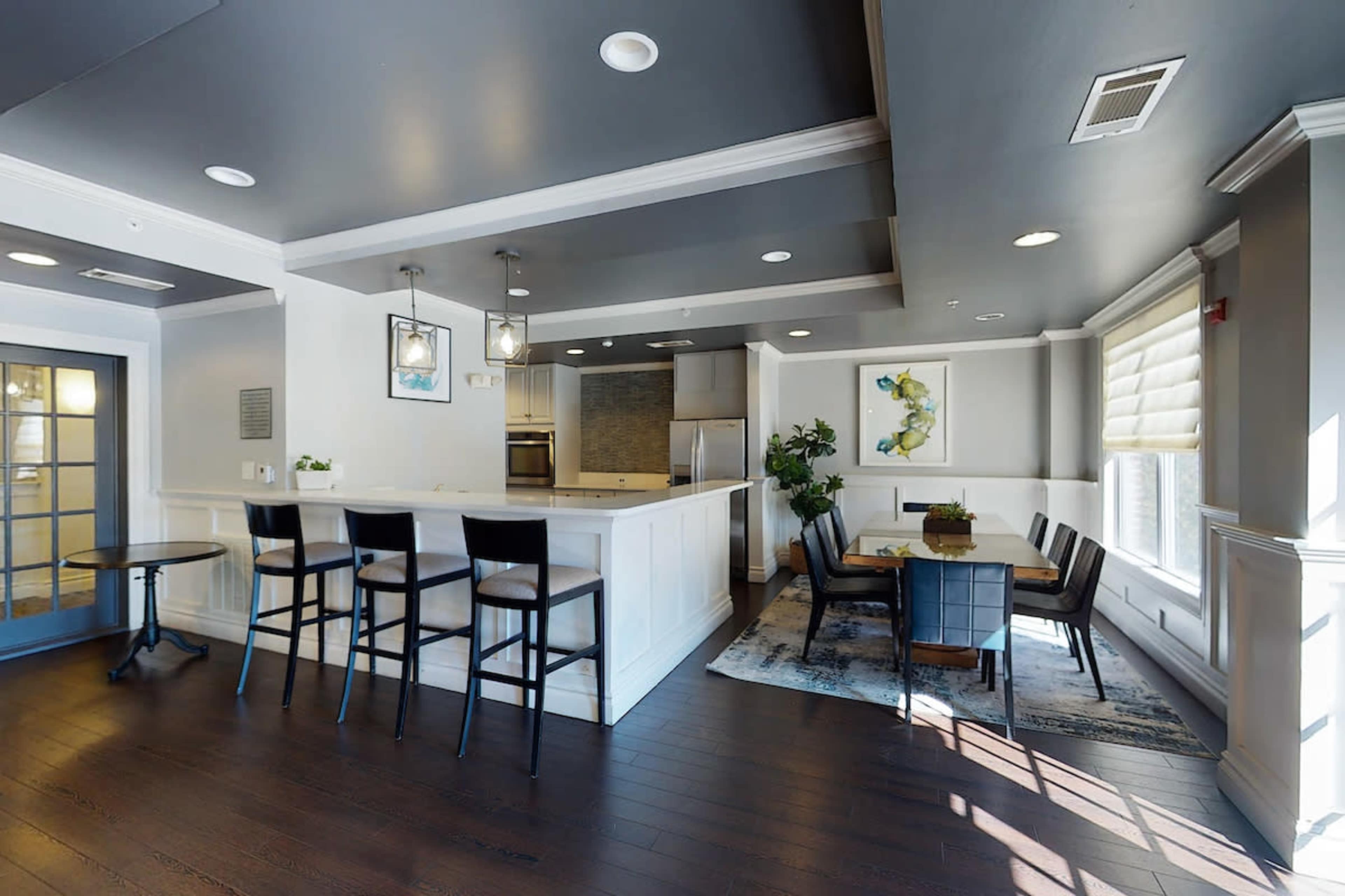 A contemporary dining area with a kitchen bar, high stools, and a dining table near a large window.