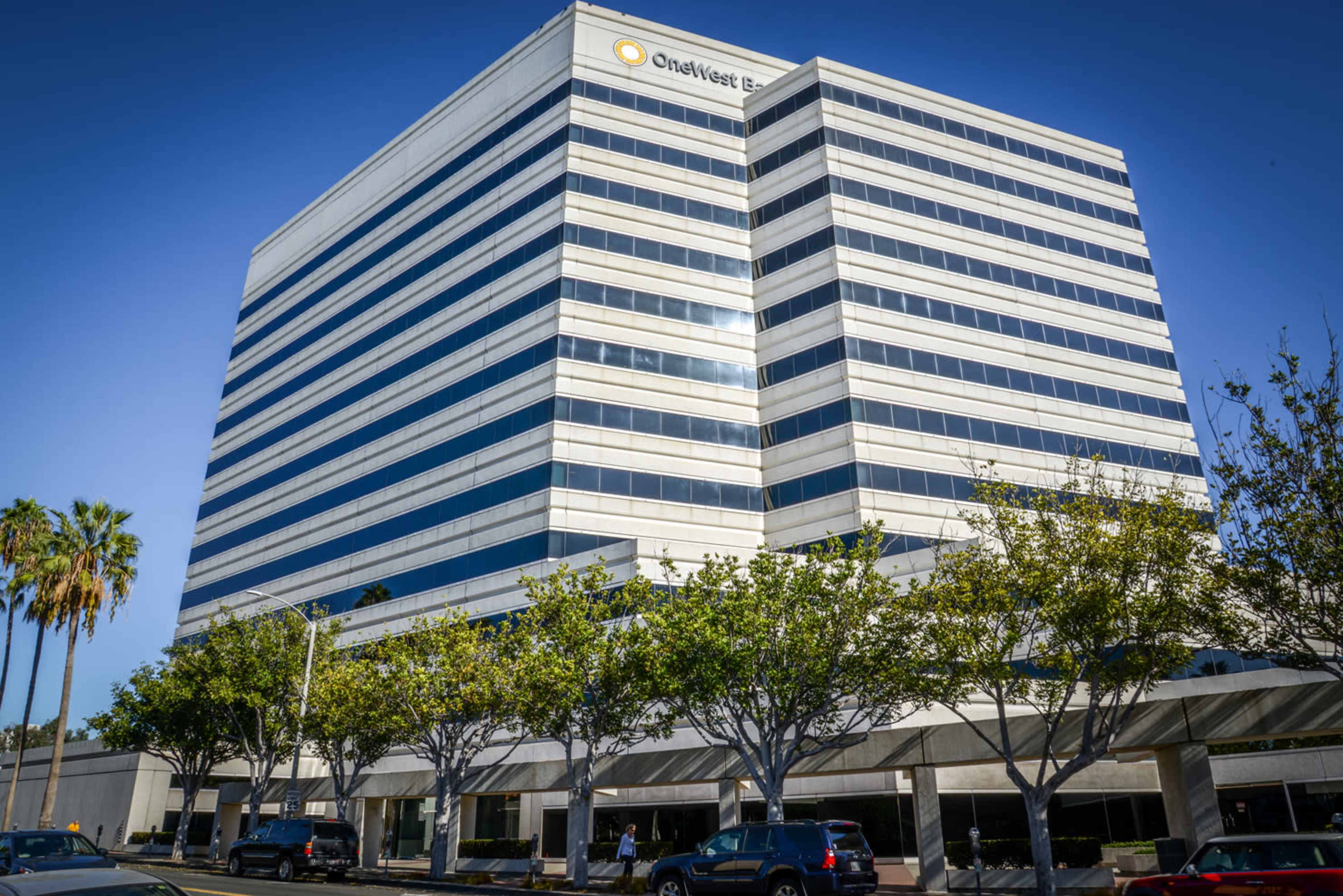 A modern multi-story office building with large windows and a sign for OneWest Bank, surrounded by palm trees and a sidewalk.