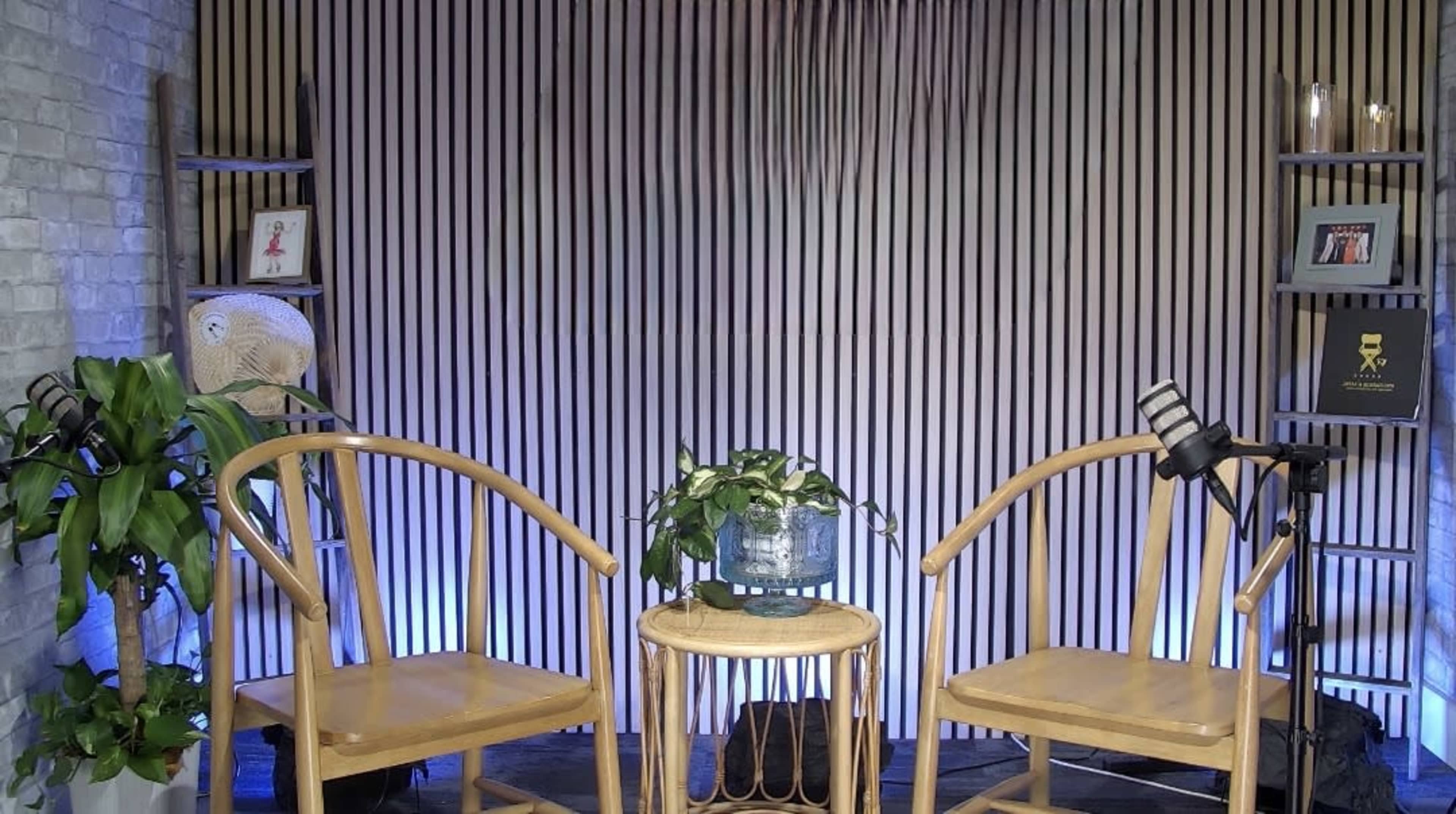 A cozy interview setup features two wooden chairs and a small round table adorned with a plant, surrounded by a backdrop of vertical wooden slats.