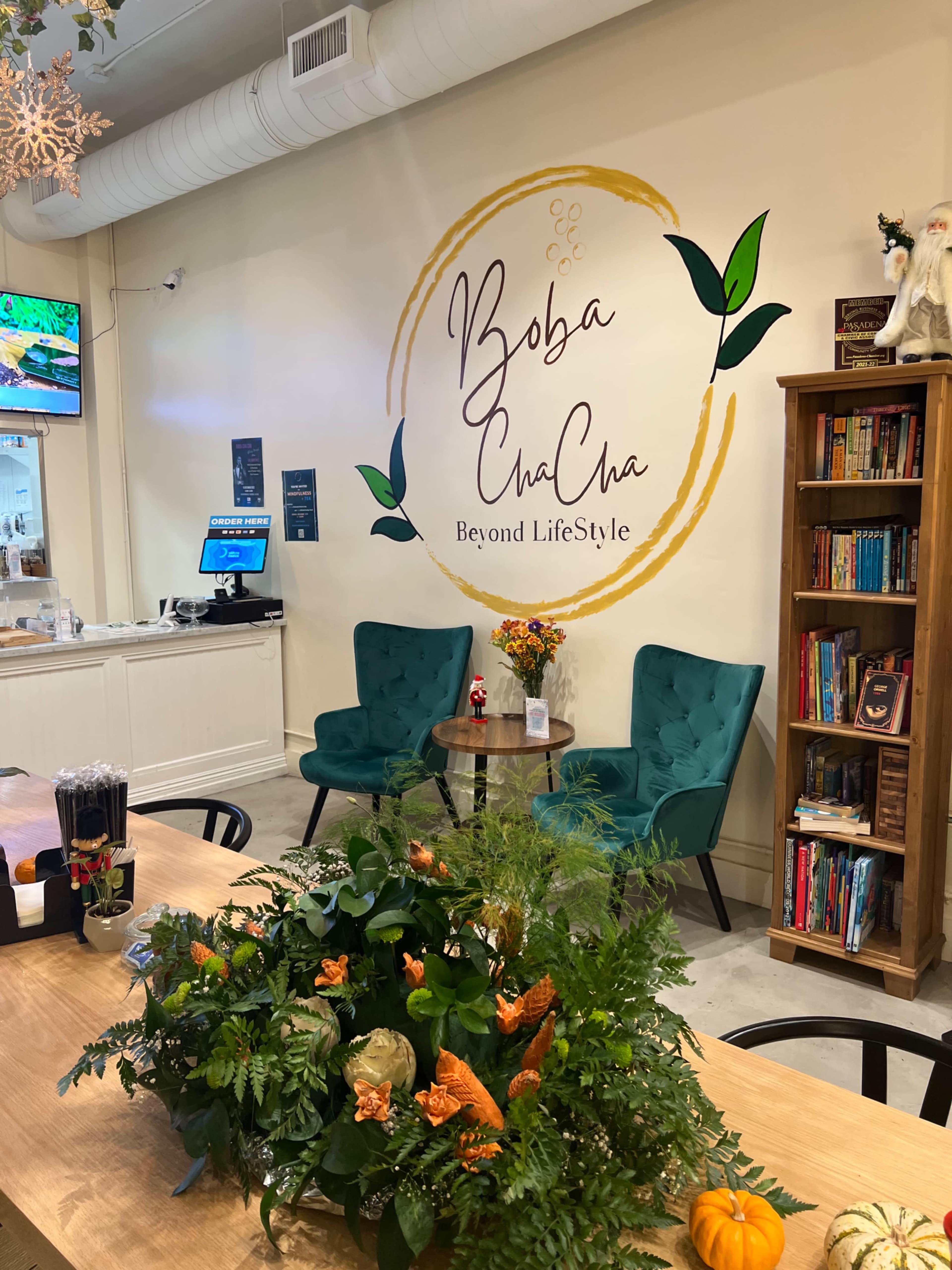 A cozy interior of a boba tea shop featuring two teal chairs, a wooden table, and a decorative wall with the shop's name and logo.
