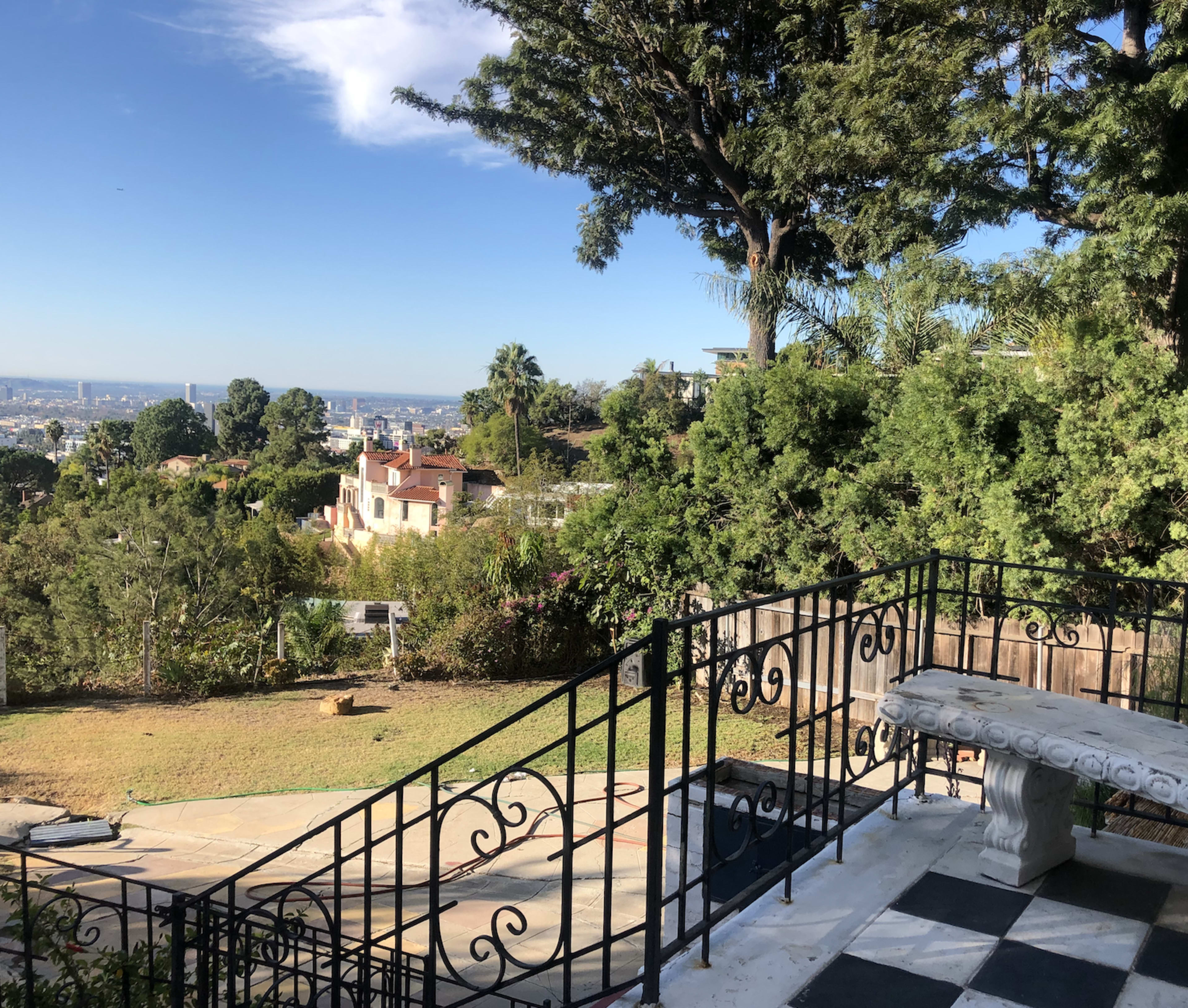 A landscaped outdoor area with a stone pathway, a wrought-iron railing, and a view of a suburban landscape and distant city skyline.