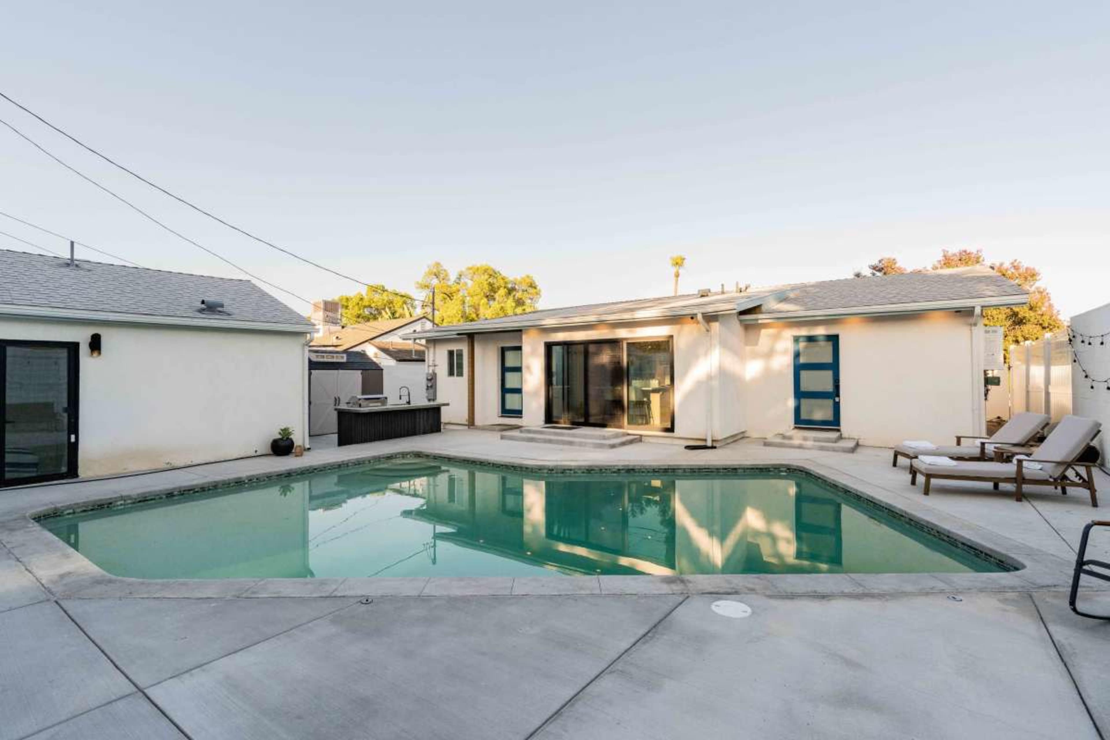 The image shows a backyard with a swimming pool in front of a single-story house featuring large sliding glass doors.