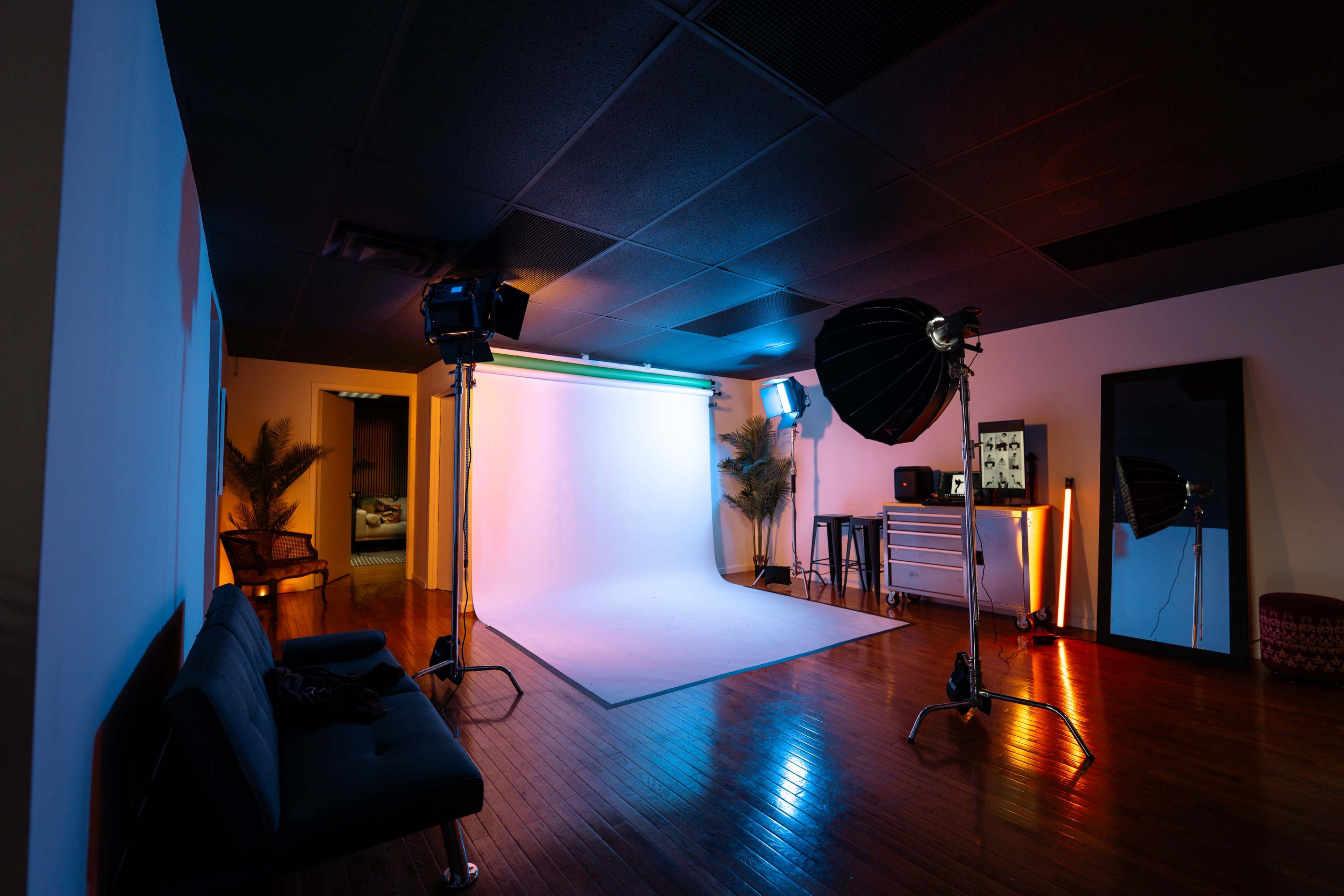 The image shows a photo studio with a backdrop, lighting equipment, and a sofa arranged within a space that includes a doorway to another room.
