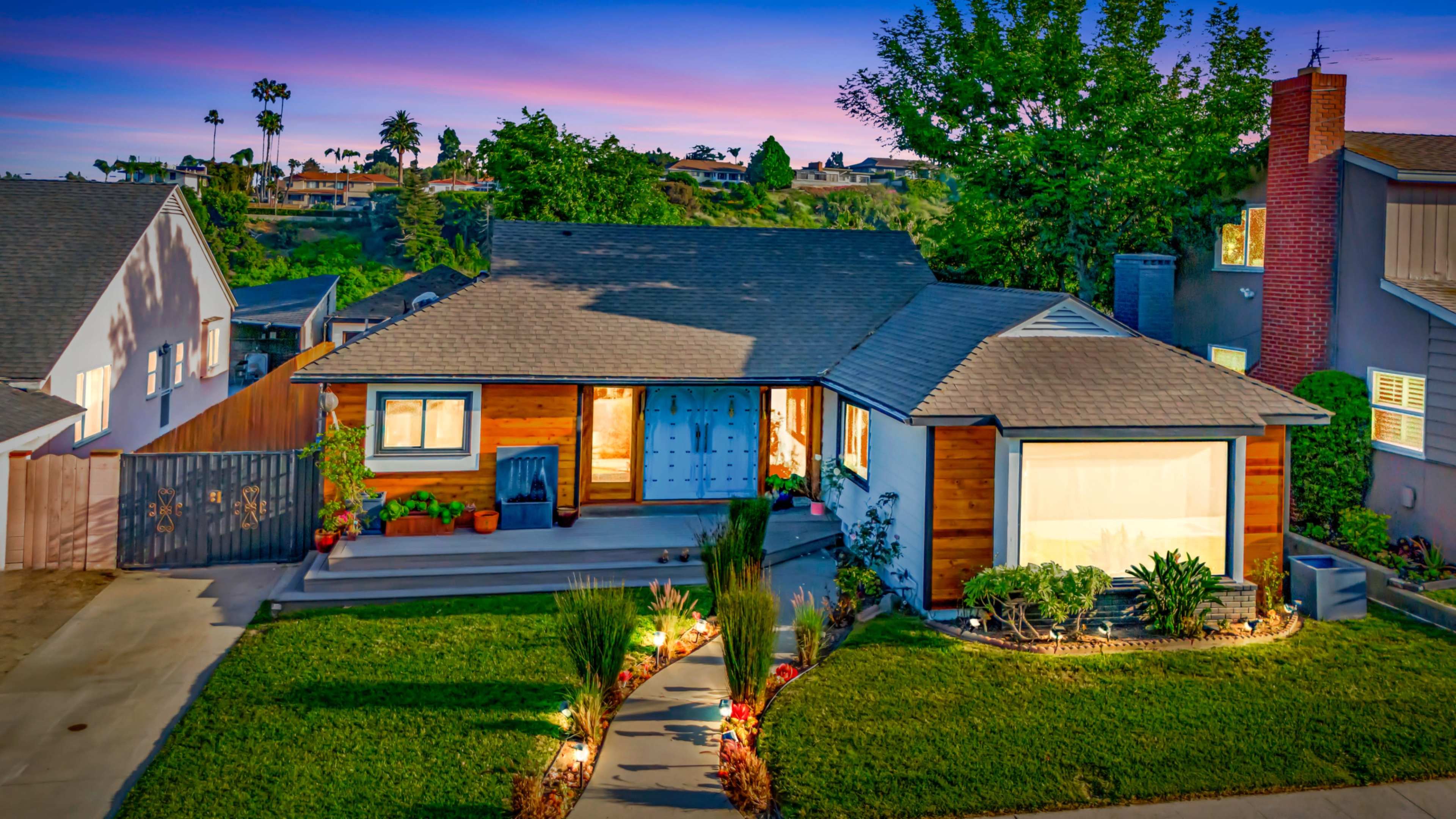 A single-story house with a wooden facade and blue double doors is set in a landscaped yard with decorative lighting and plants.