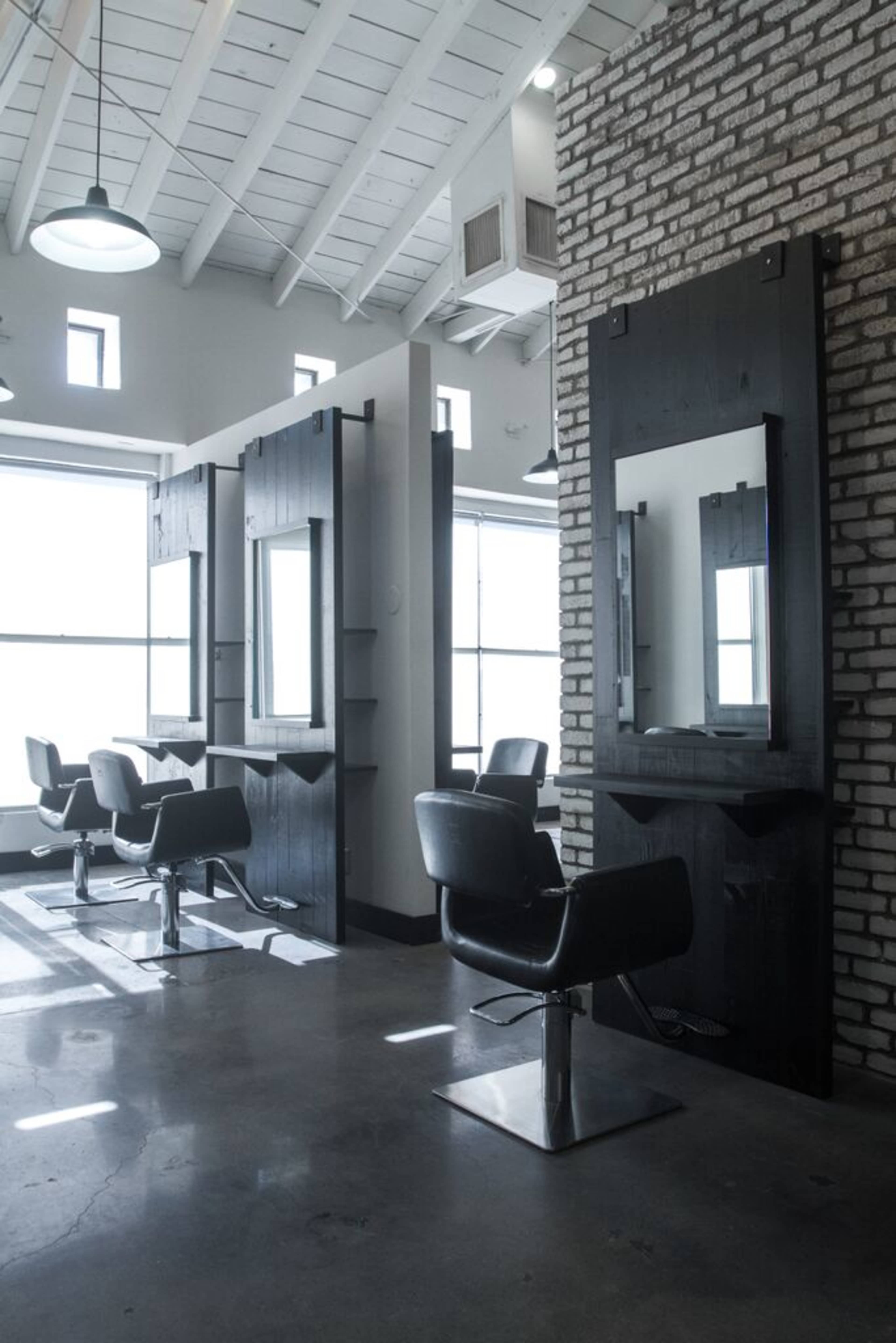 The image shows a modern hair salon with black styling stations and two black chairs arranged in a spacious, well-lit interior.