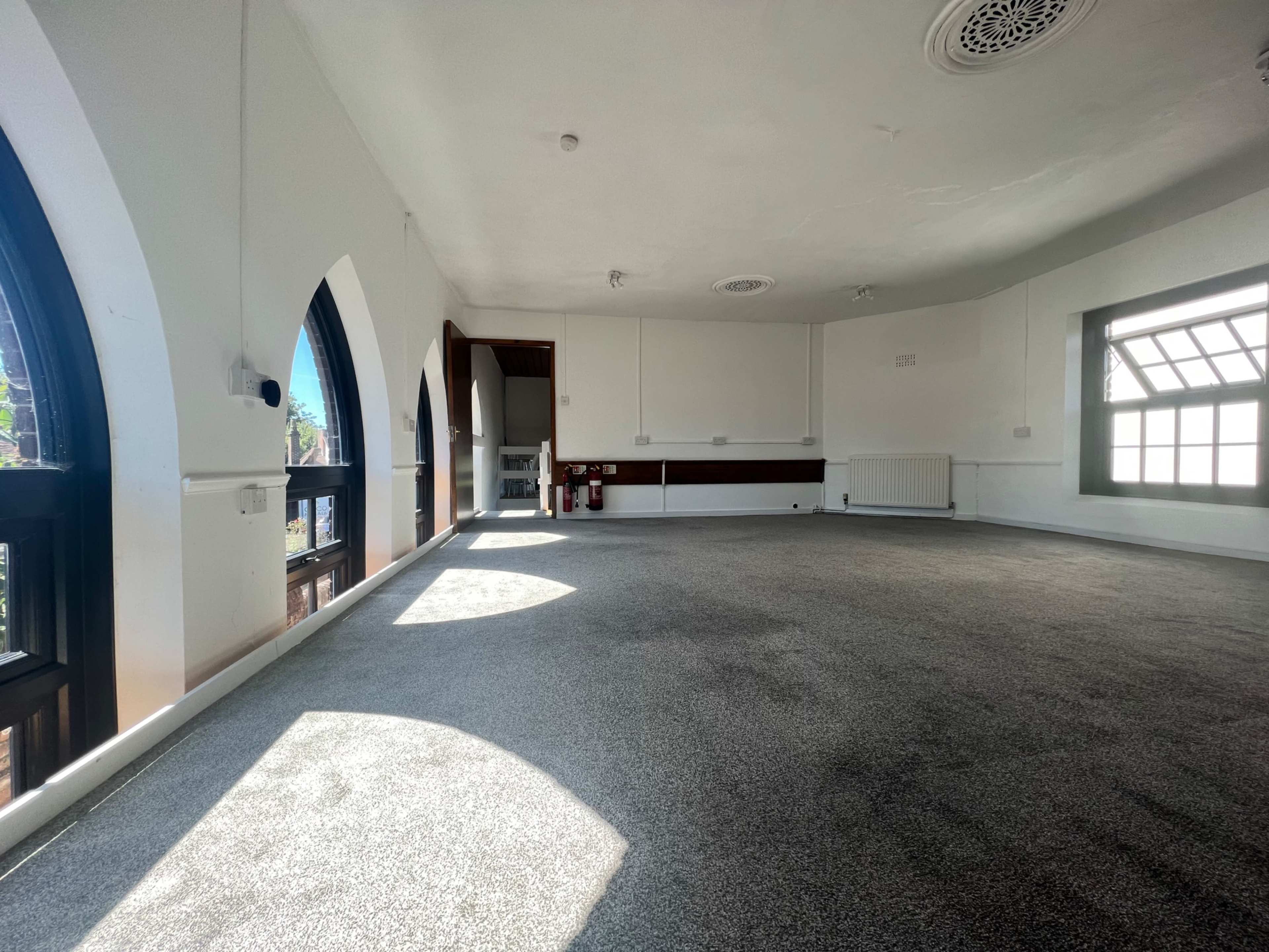 An empty room with arched windows, light-colored walls, and a carpeted floor.