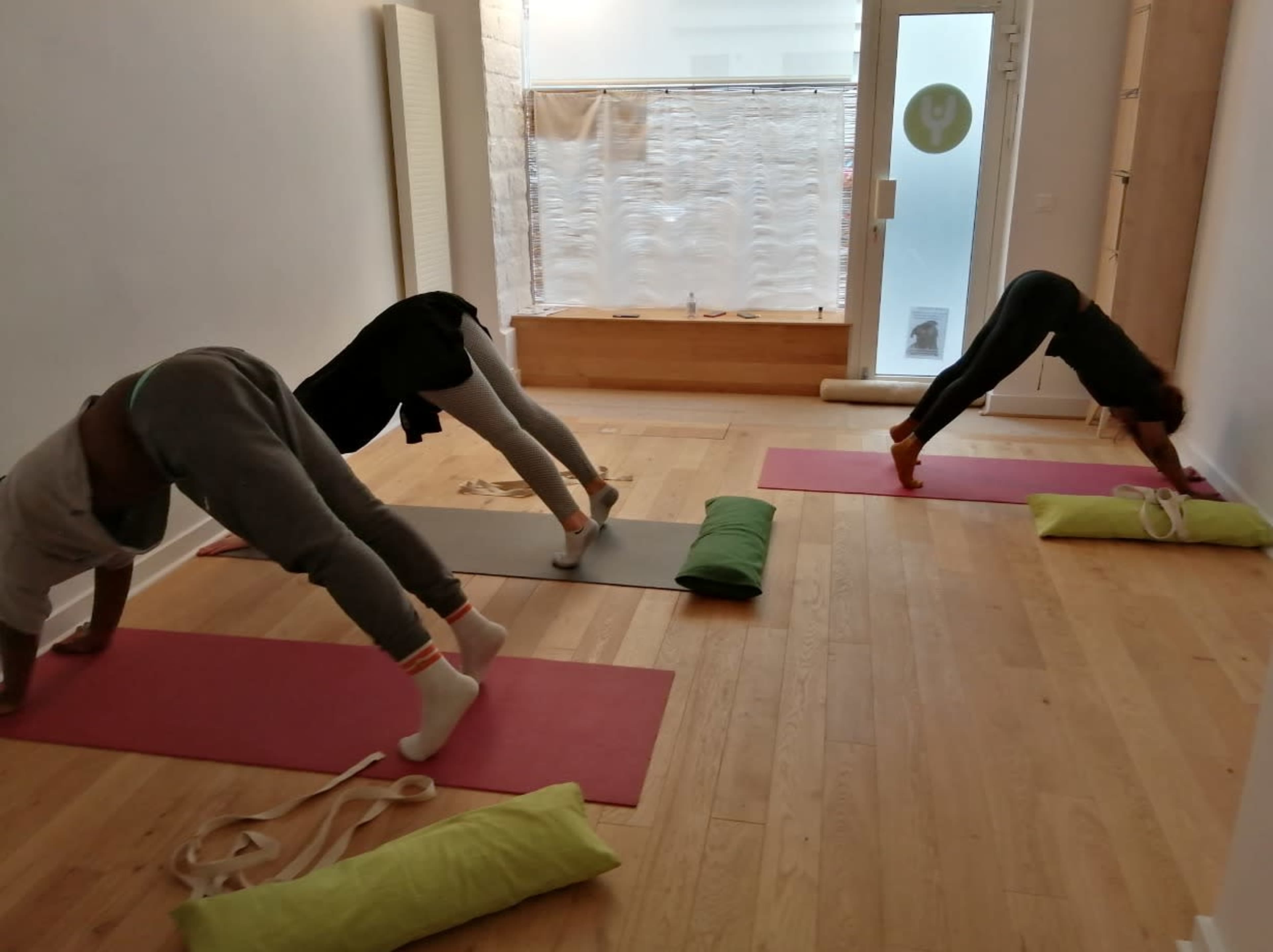 Three individuals practice downward dog yoga poses on mats in a light-filled studio.