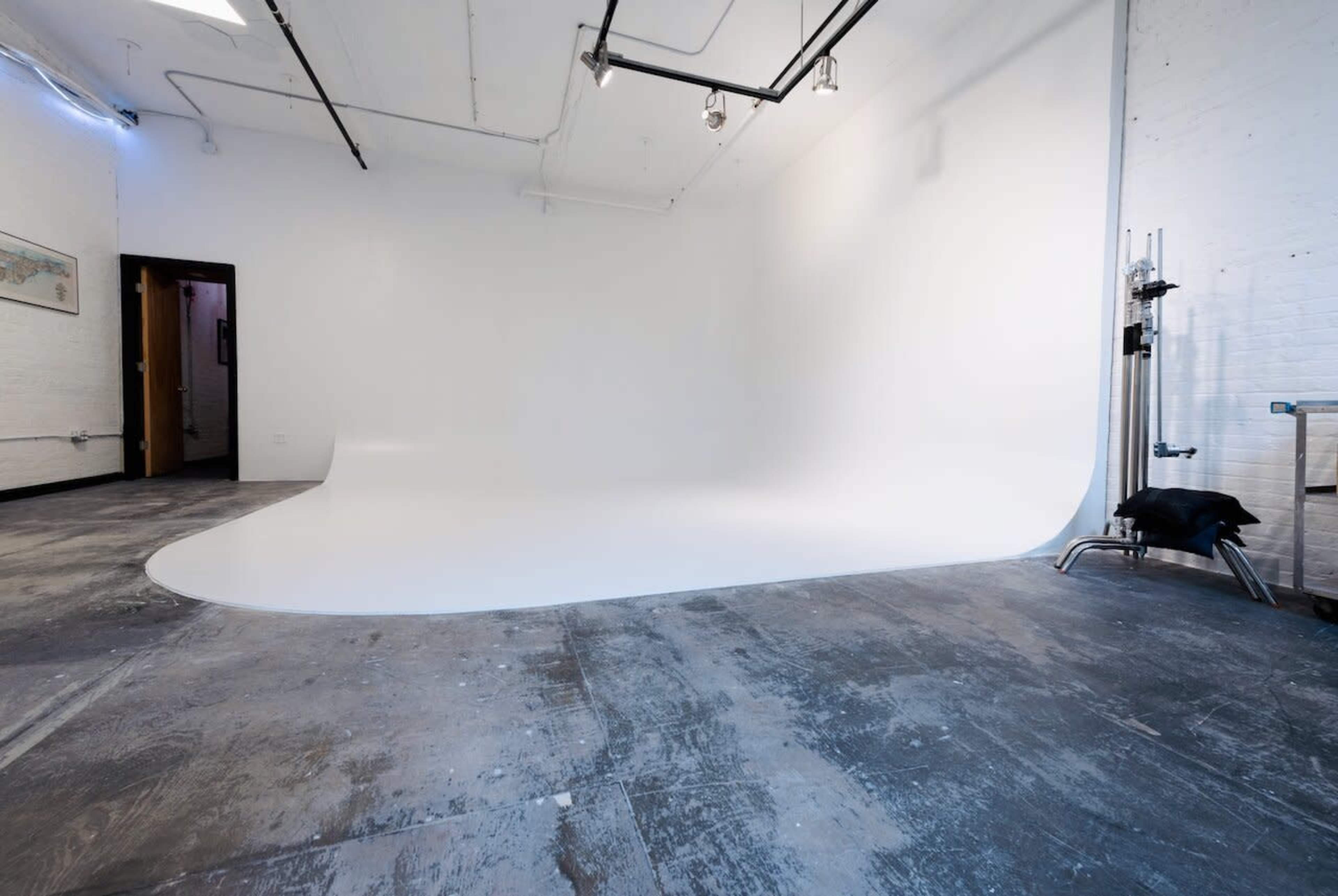 A spacious photography studio with a seamless white backdrop and concrete flooring.