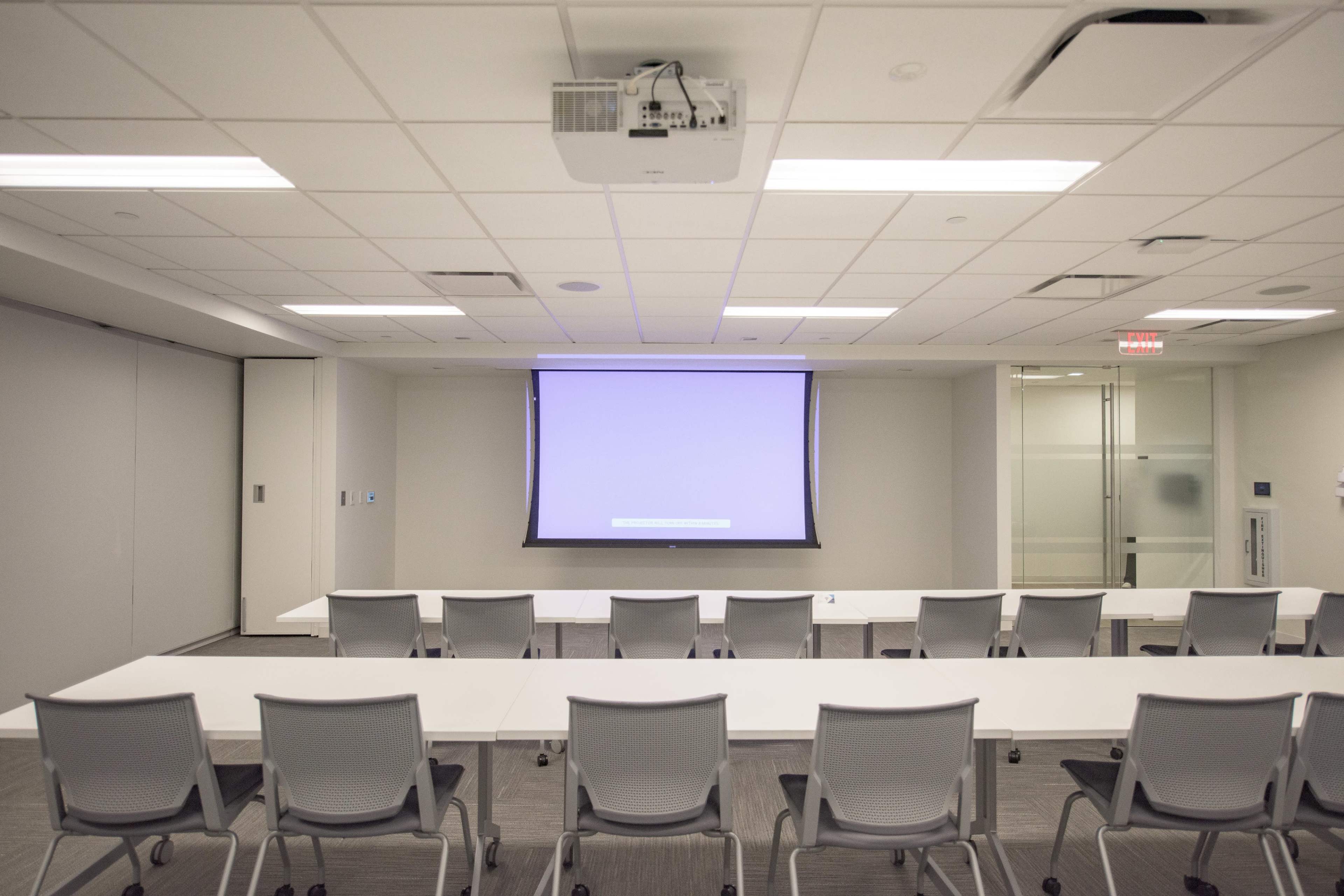 A modern conference room features rows of chairs arranged in front of a large screen and white tables.
