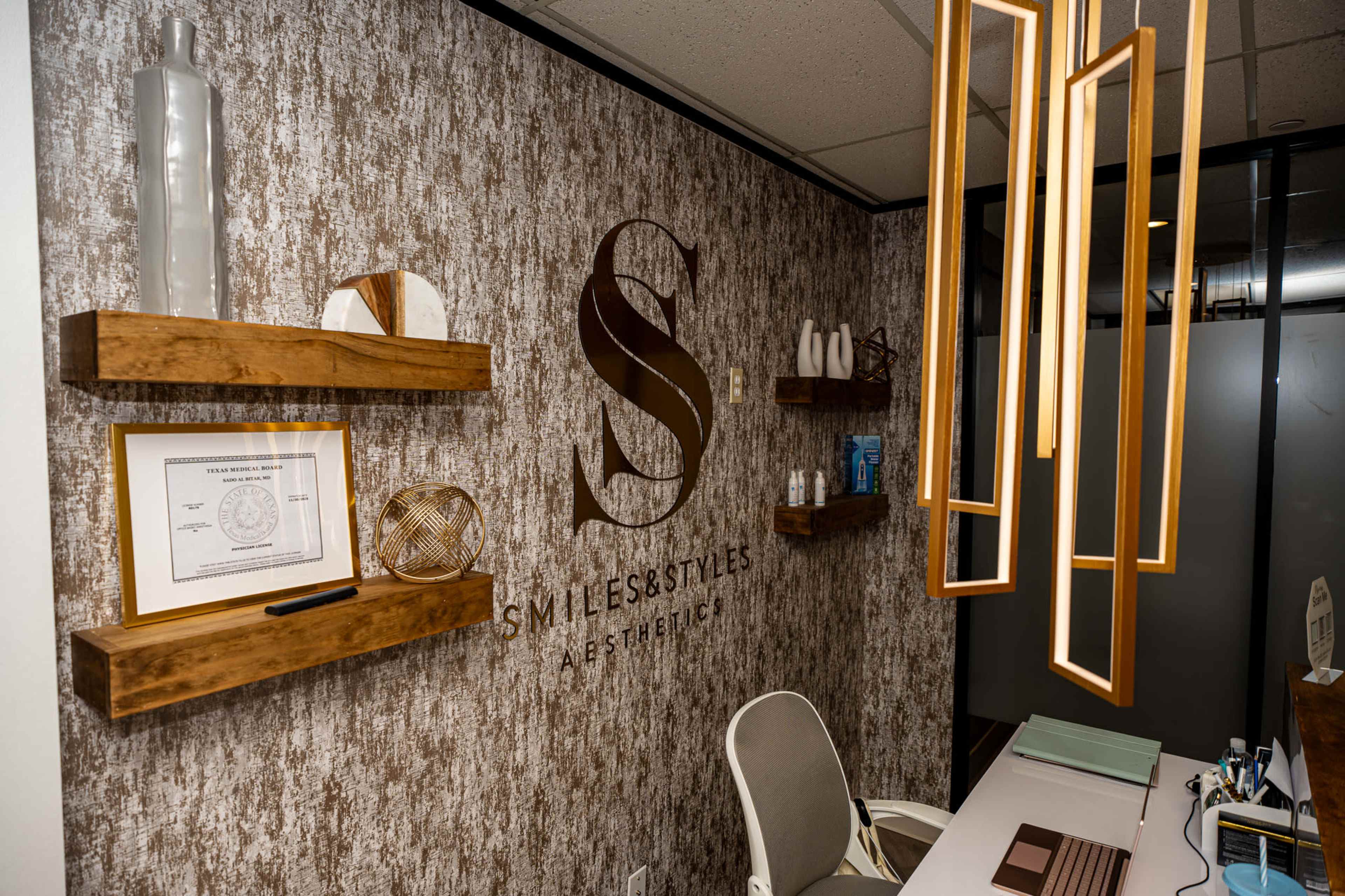 The image features a modern reception area with wooden shelves displaying decorative items, a chair, and a wall adorned with a logo that reads "SMILES & STYLES AESTHETIC."