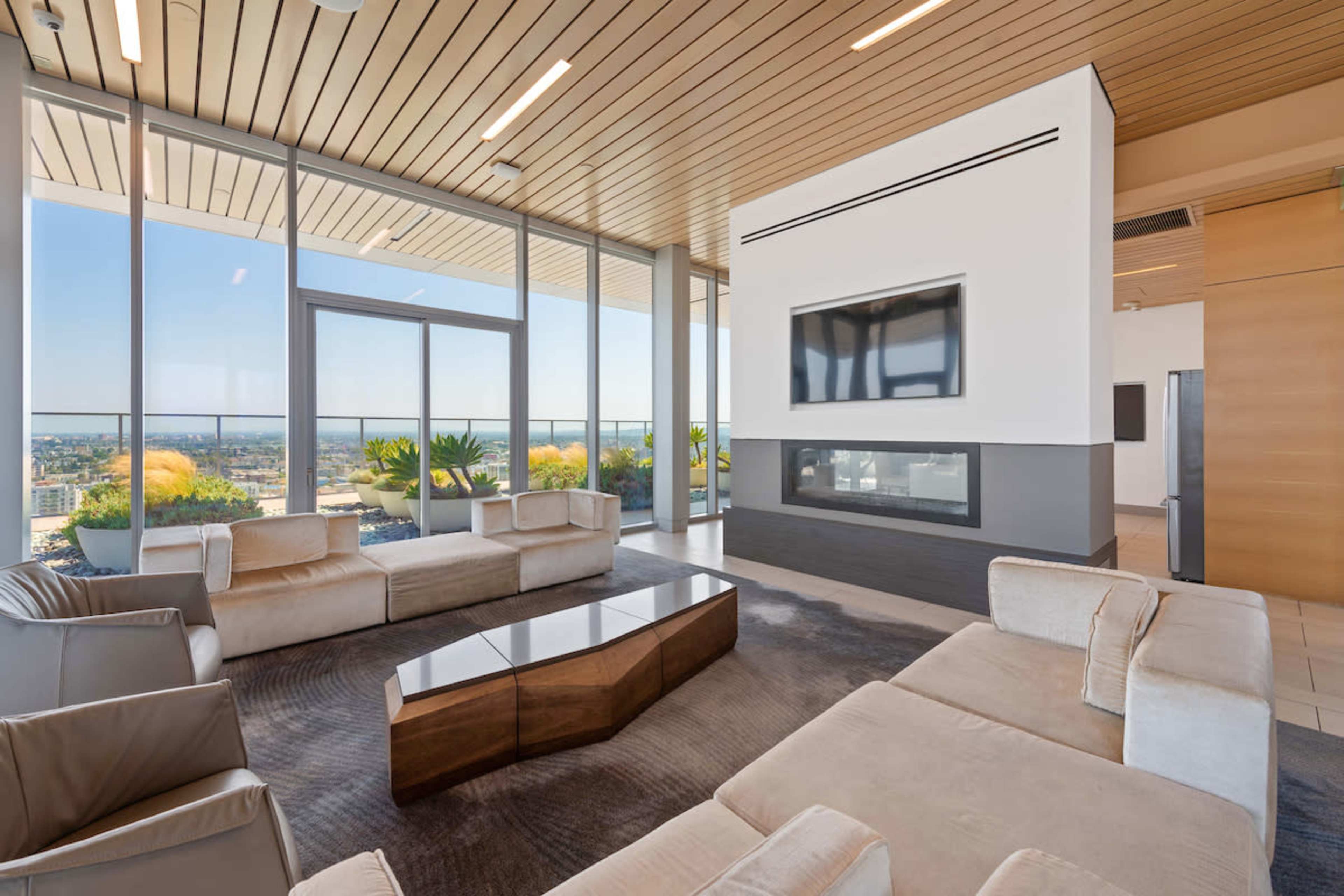 A modern living room with large windows, a linear fireplace, and contemporary furniture arranged around a geometric coffee table.