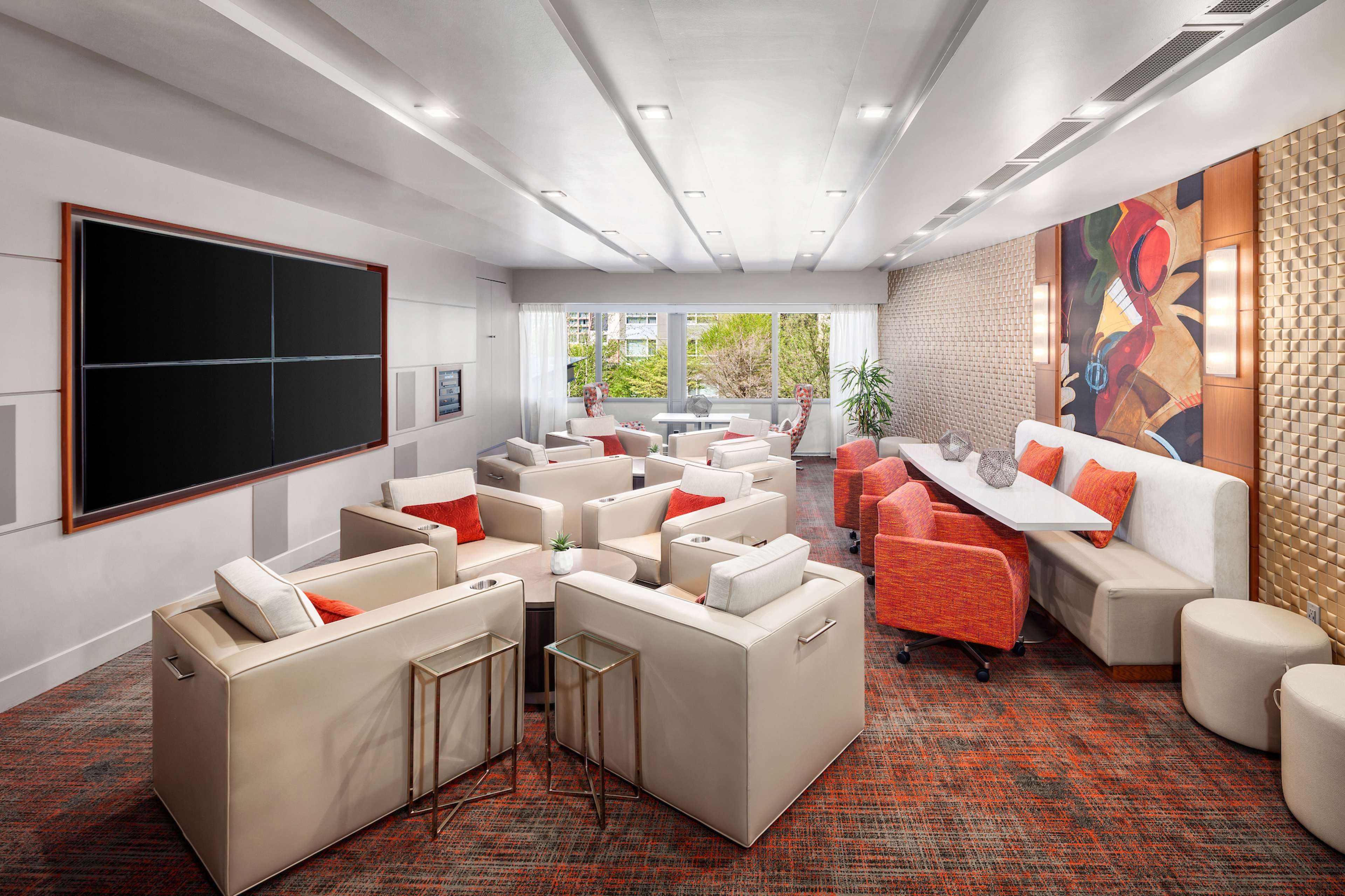 A modern lounge area featuring white and orange seating, a large flat-screen TV, and a decorative wall panel.