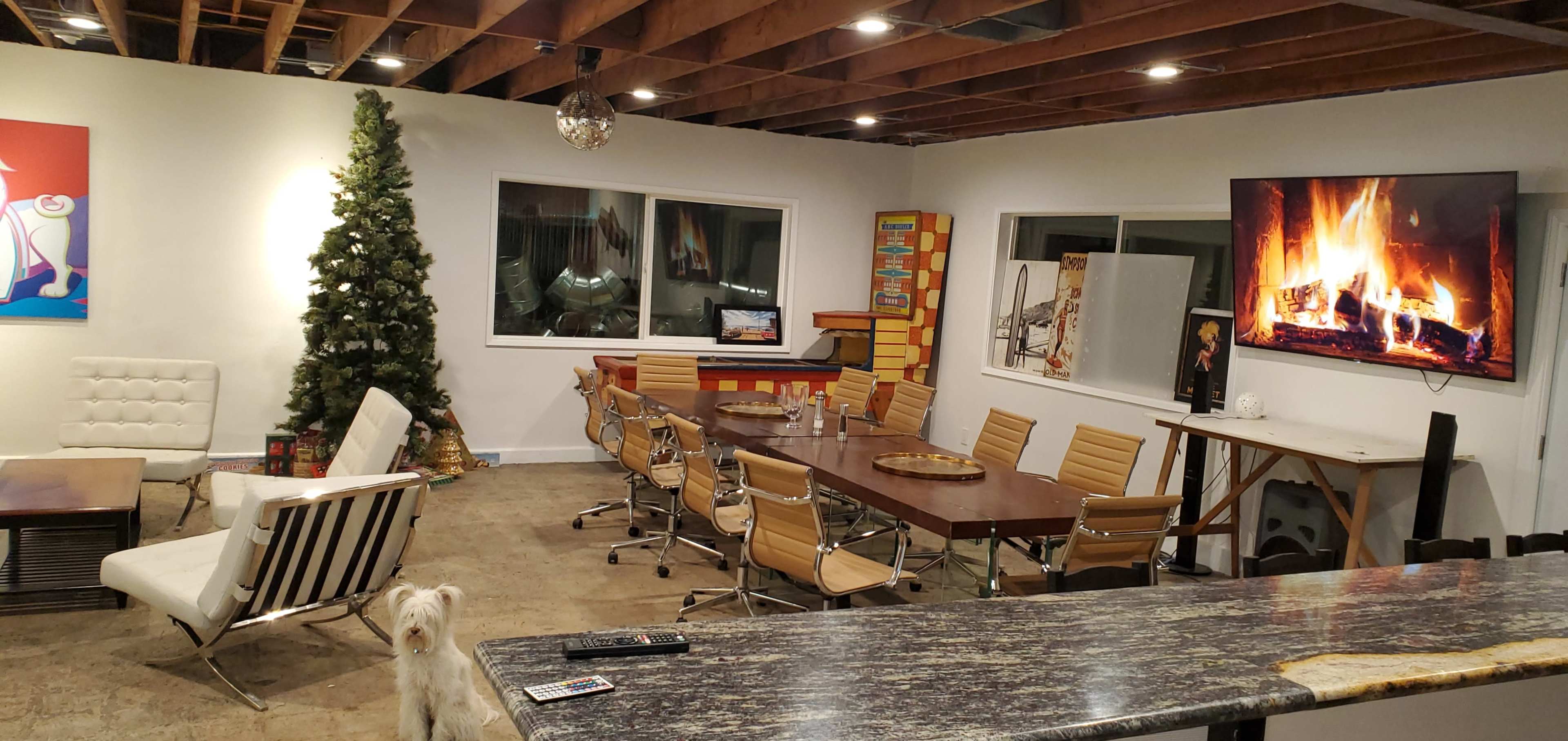 The image depicts a modern meeting room with a large wooden table, several chairs, and a decorative Christmas tree in the corner, featuring a wall-mounted TV displaying a fireplace.