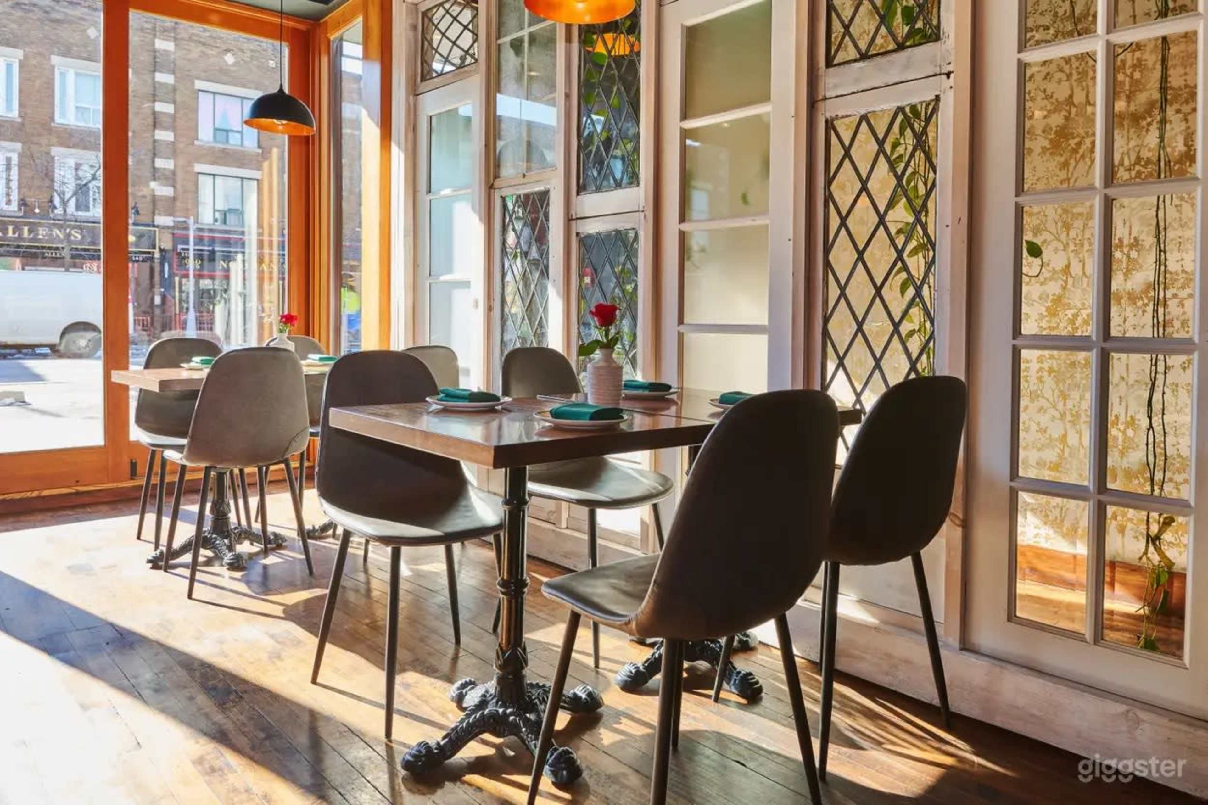 A cozy restaurant interior features wooden tables, chairs, and large windows allowing natural light to fill the space.