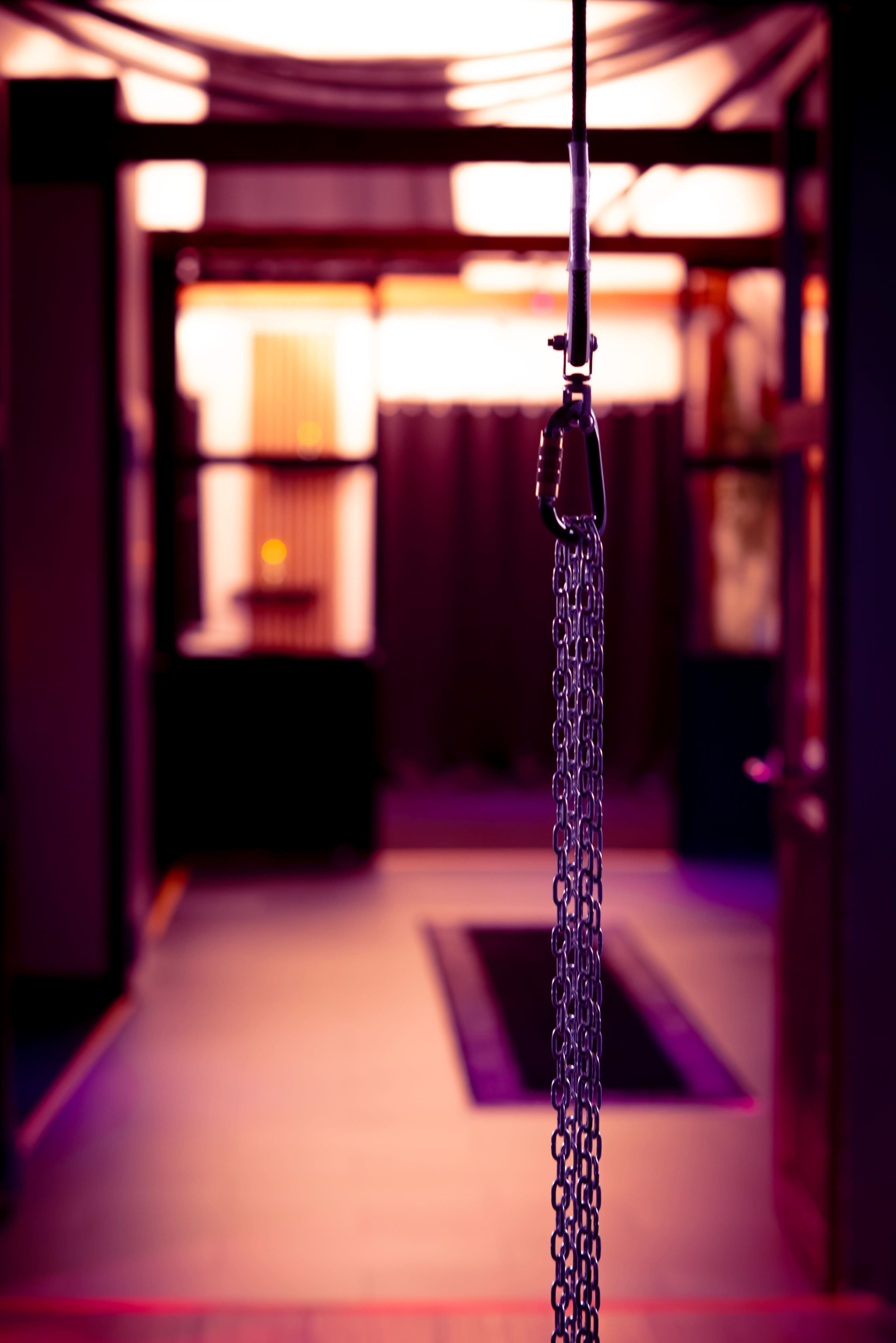 A metal chain hangs from a pulley in a dimly lit corridor with blurred colorful lighting.