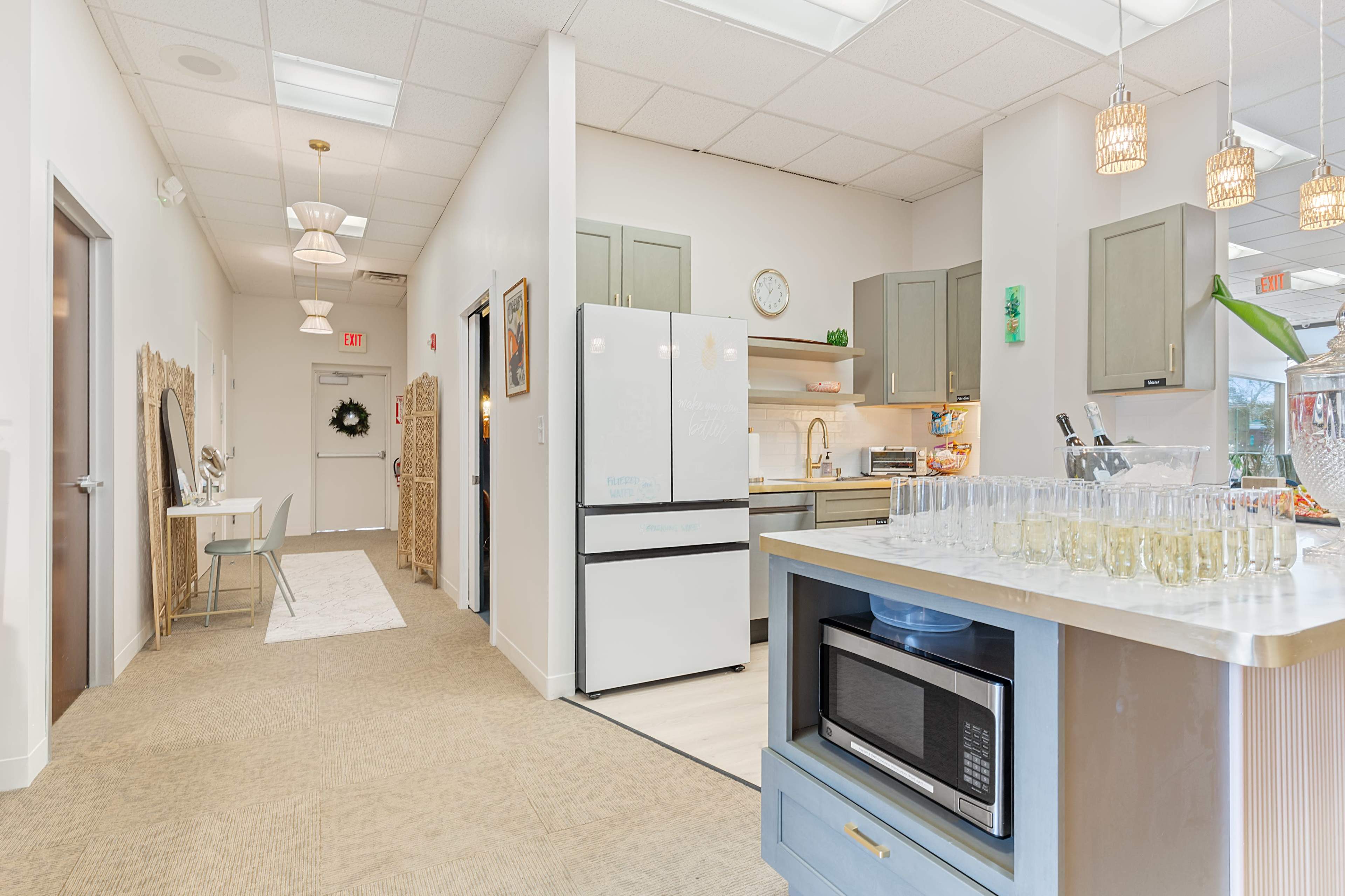 The image shows a modern kitchen area with a dining space, featuring light-colored cabinets and a bar counter with glasses arranged on it.