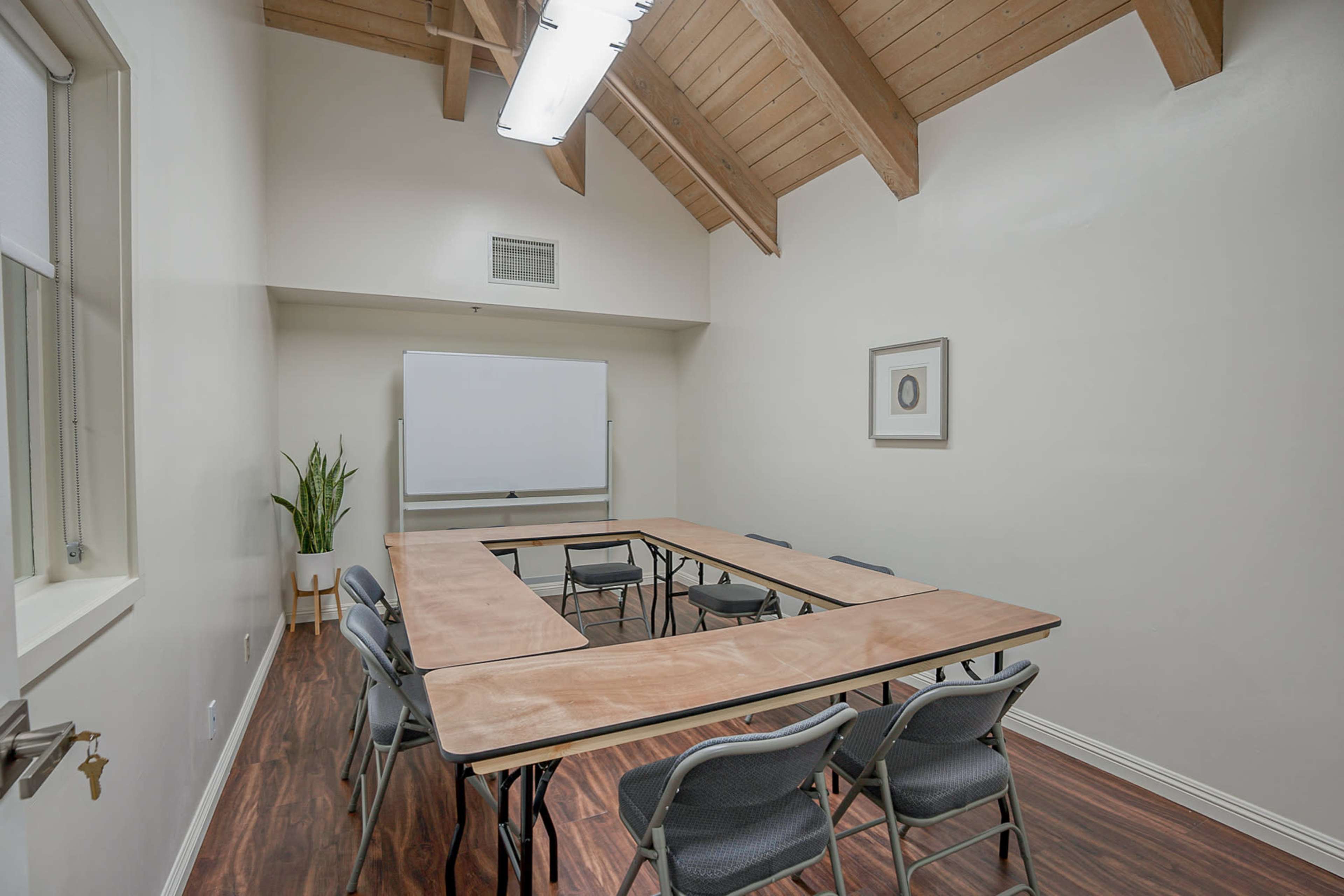 A conference room with a wooden table arranged in a U-shape, surrounded by gray chairs and featuring a whiteboard at the front.