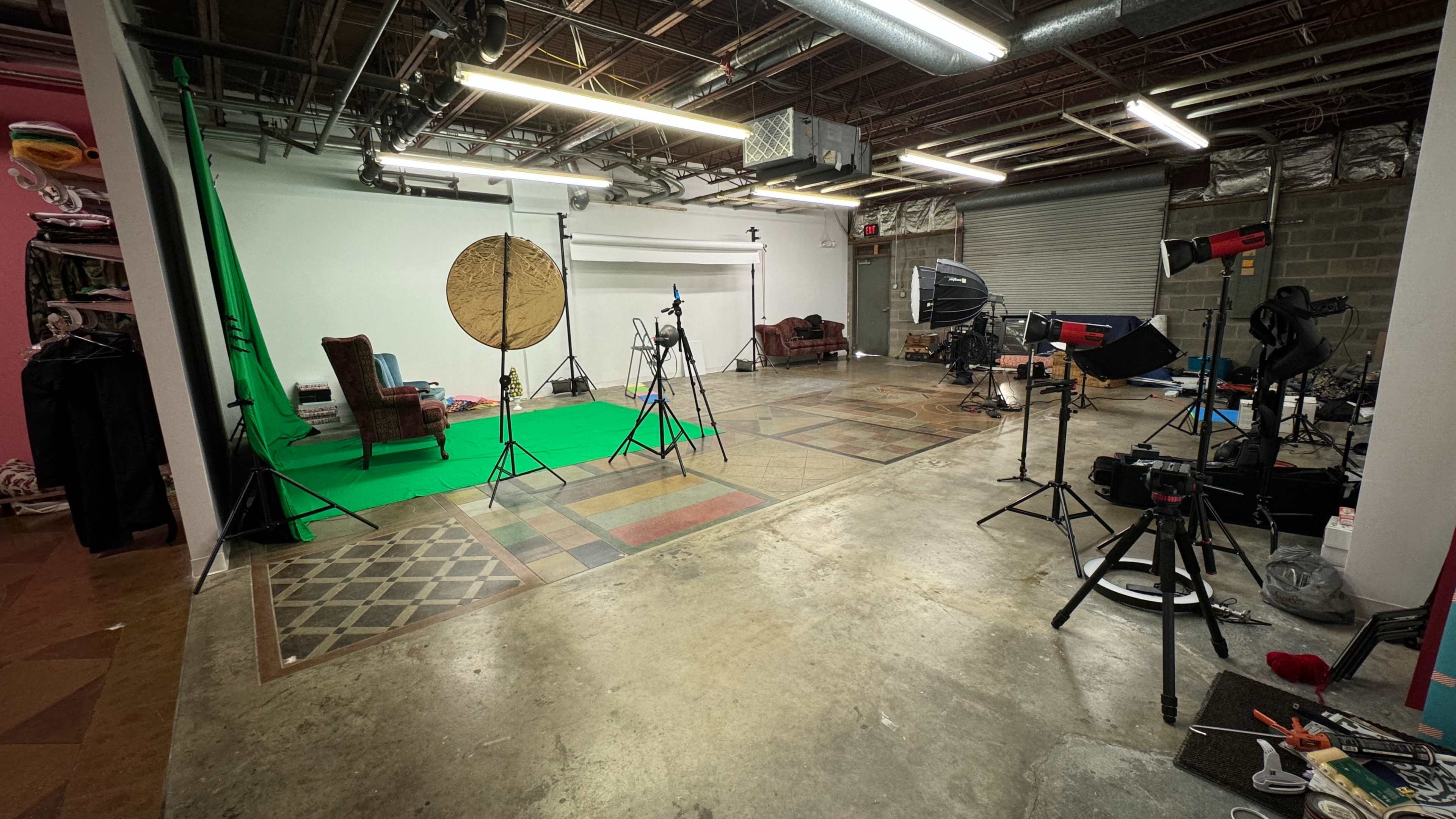 A photography studio with a green backdrop, lighting equipment, and various props arranged around a concrete floor.