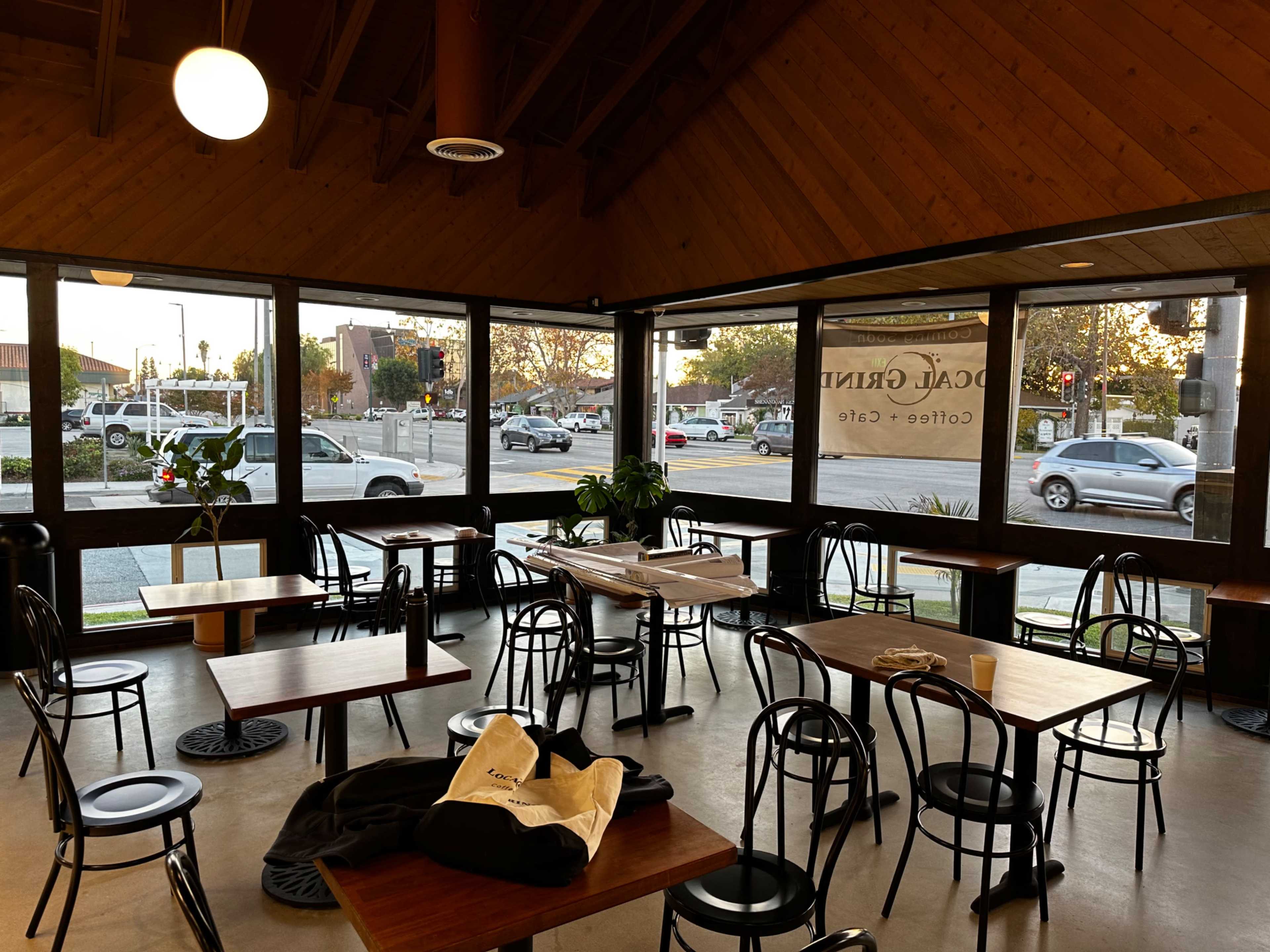 An interior of a café with wooden ceilings, several tables and chairs, and large windows facing a street.