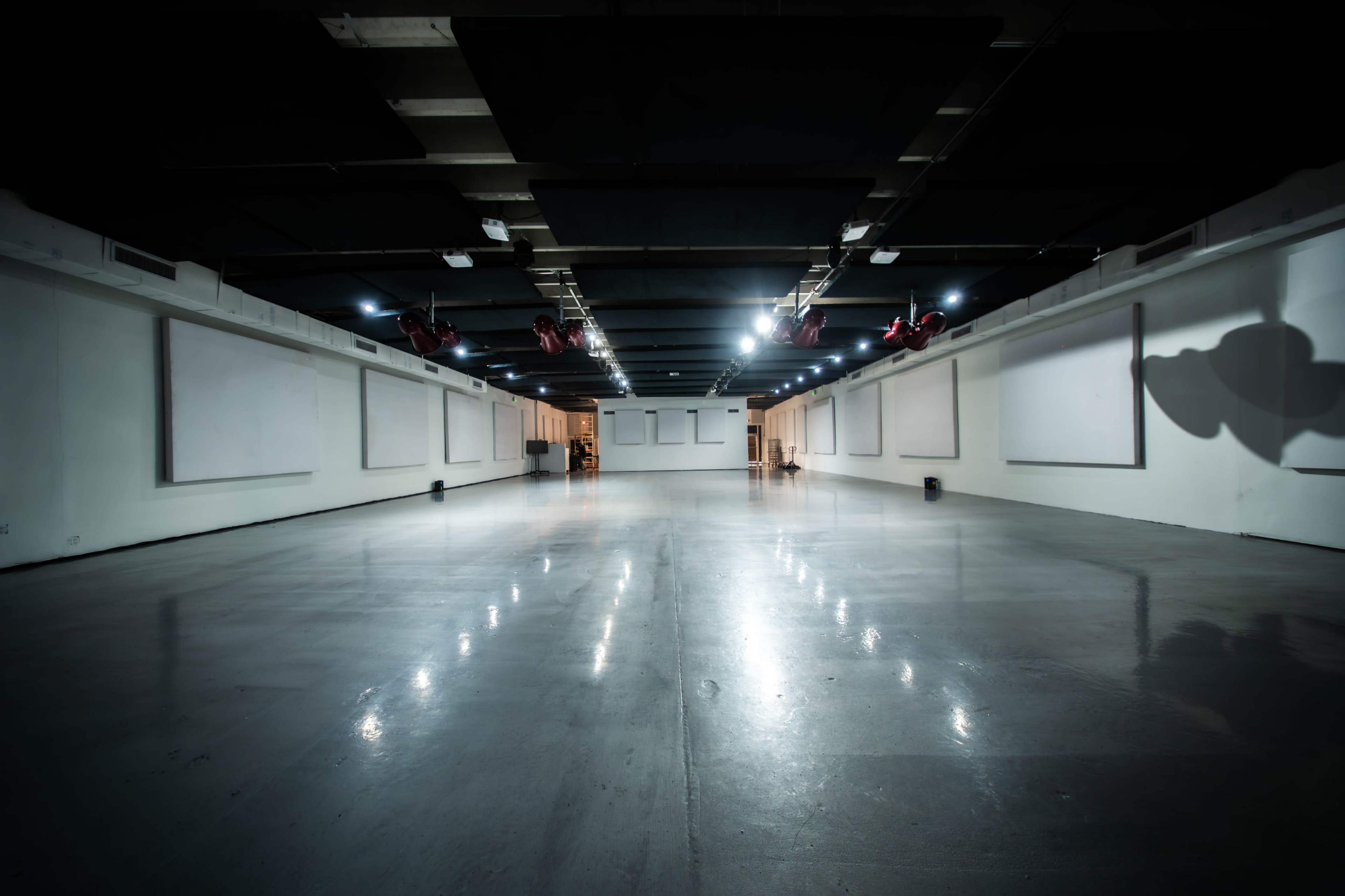 The image shows a spacious, empty room with polished concrete floors and several overhead lights illuminating the area.