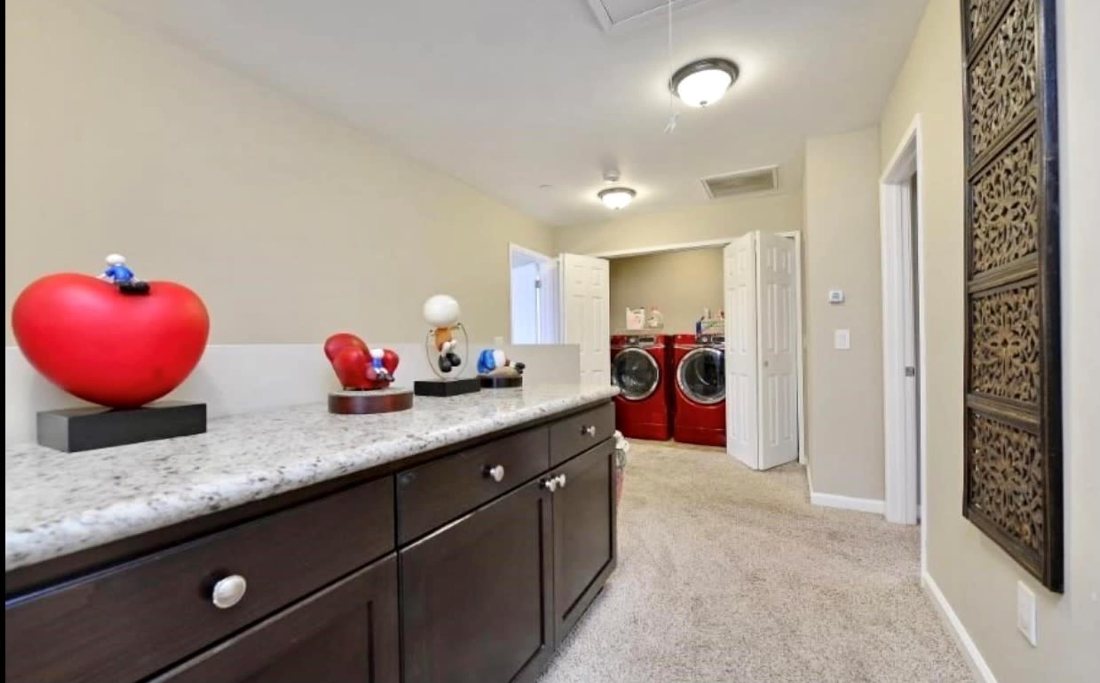 A hallway with a countertop and decorative objects, leading to a laundry room featuring red washing machines.